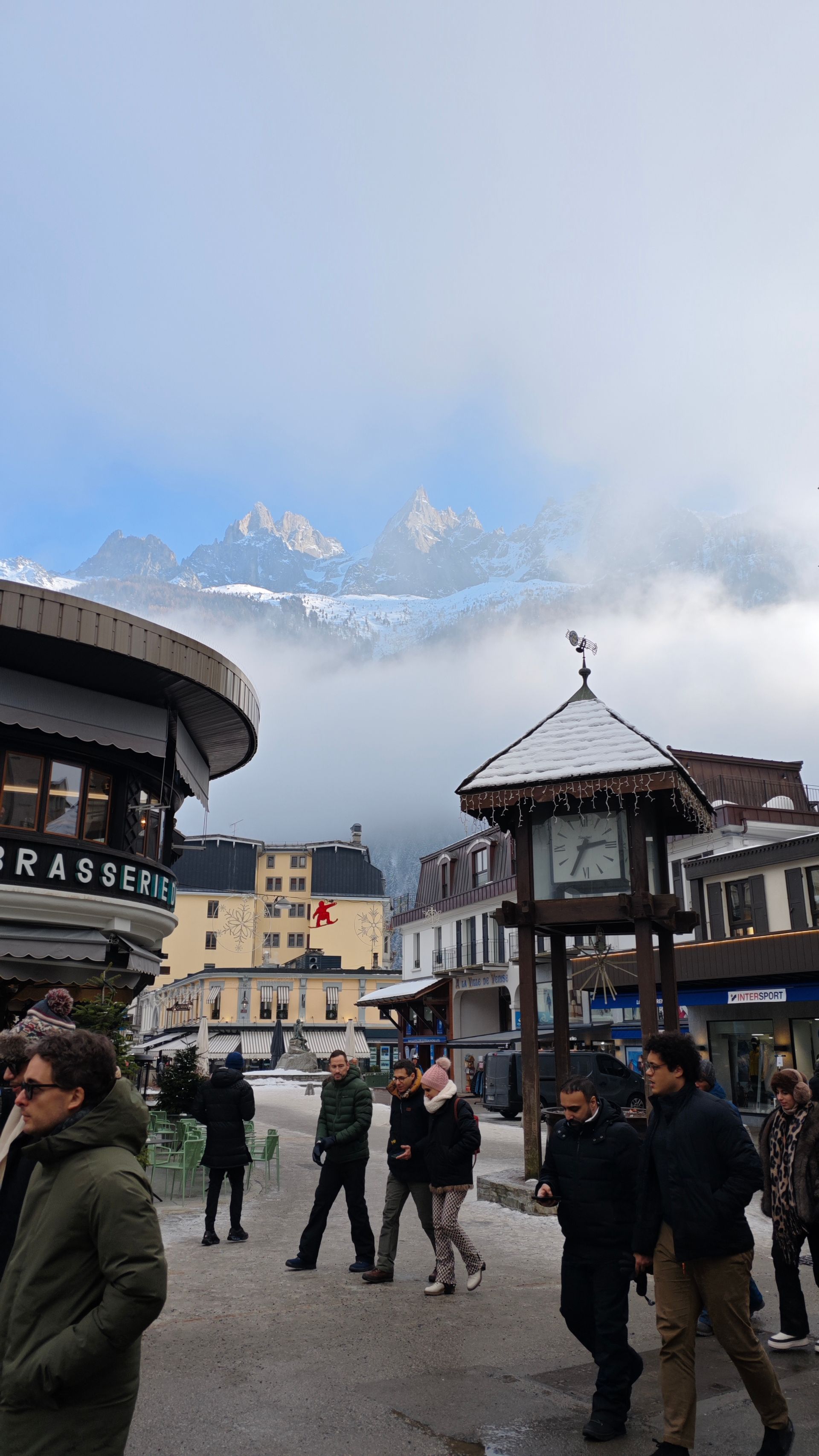 A group of people are walking down a street with mountains in the background.