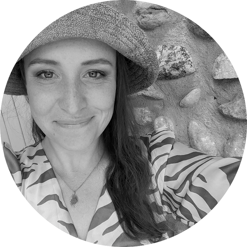 A woman wearing a hat and a zebra print shirt is smiling in a black and white photo.