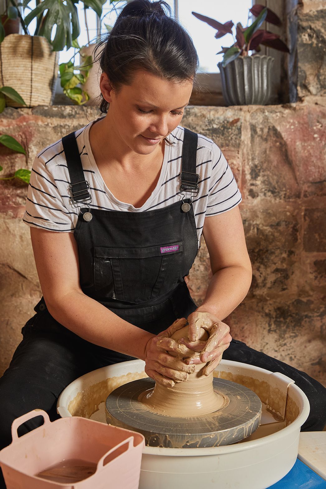 A woman is sitting on a pottery wheel making a pot.
