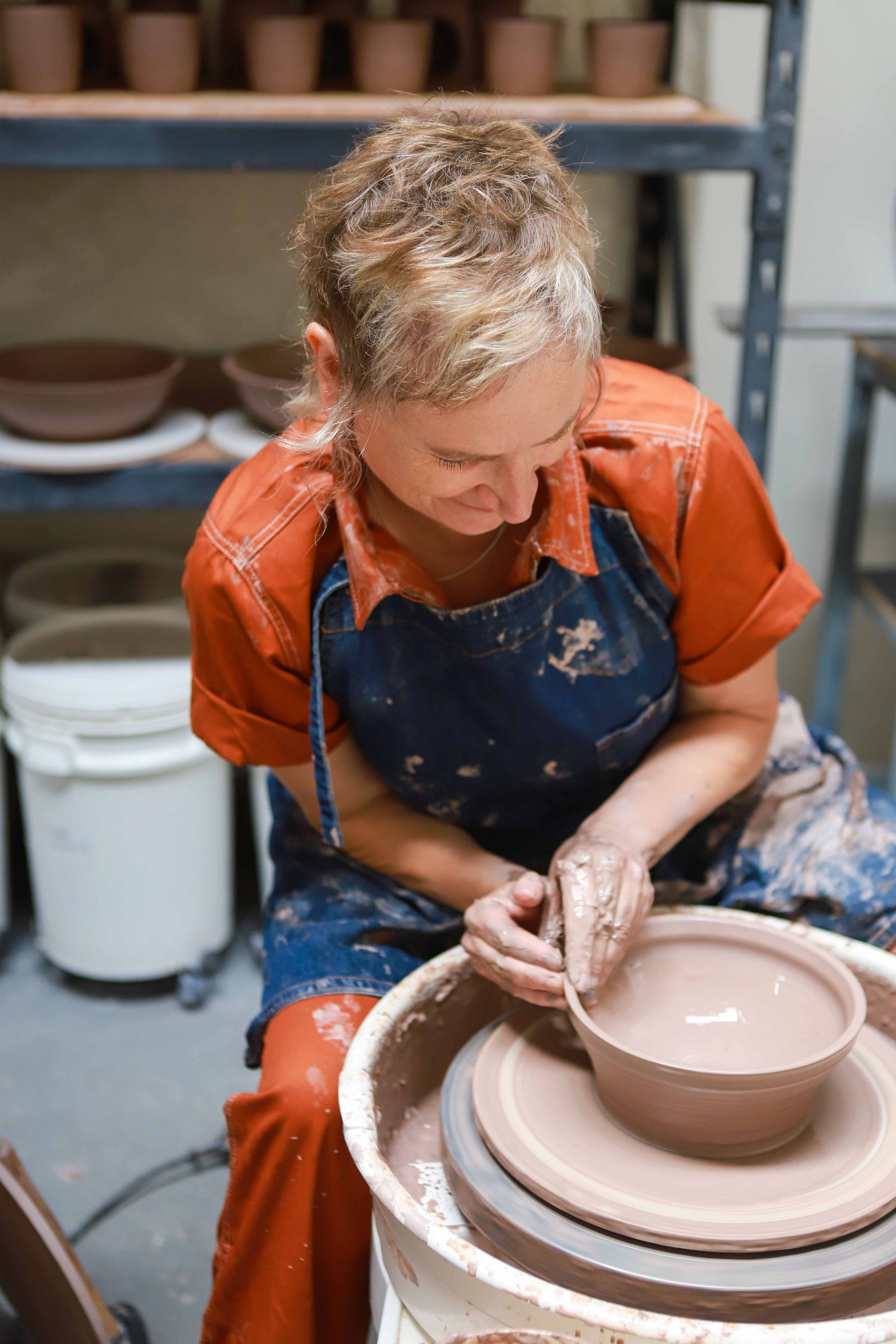 A woman is sitting on a pottery wheel making a bowl.