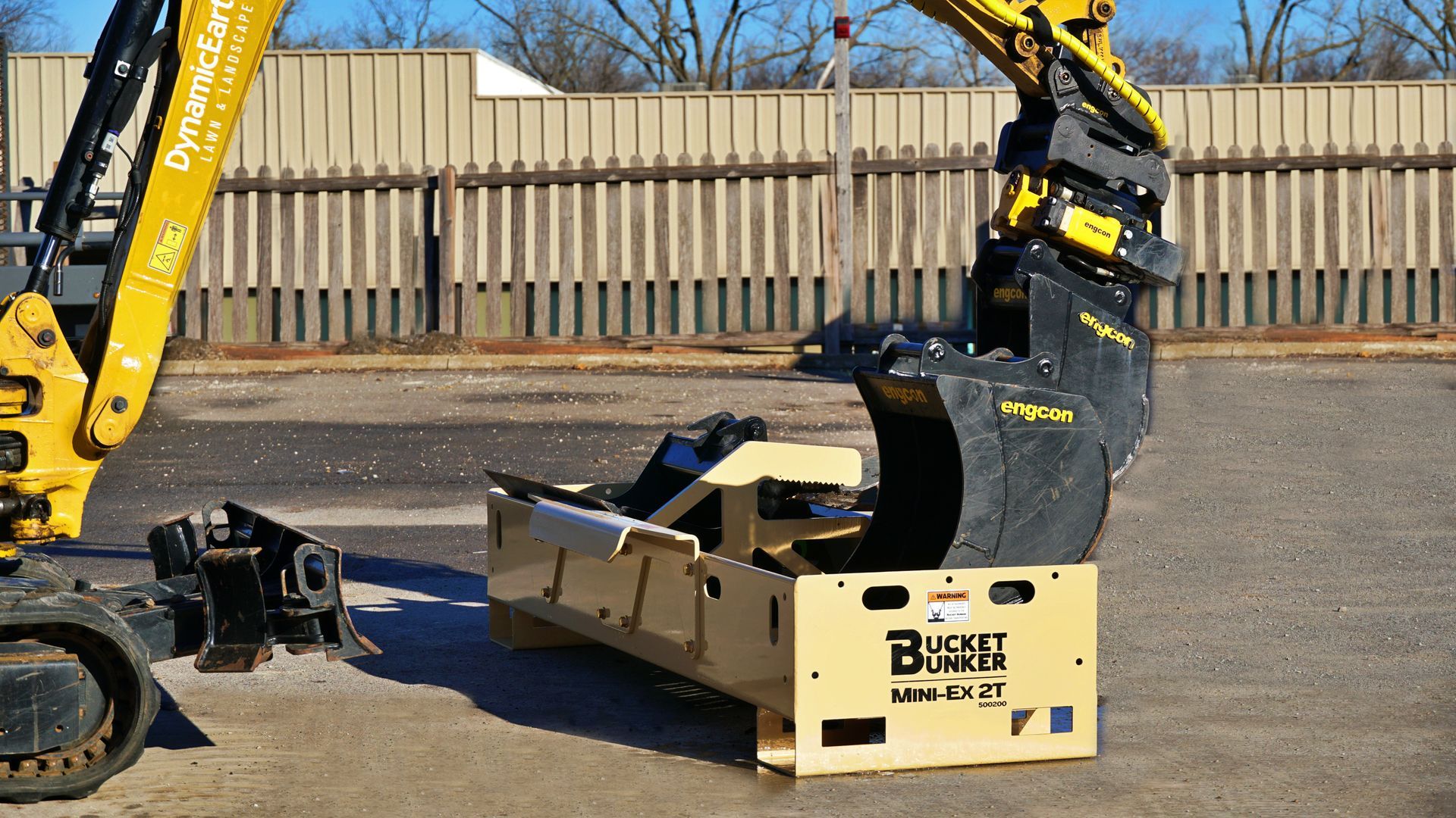 A bucket bunker mini-ex 2t has buckets in it and is sitting Infront of a mini-excavator.