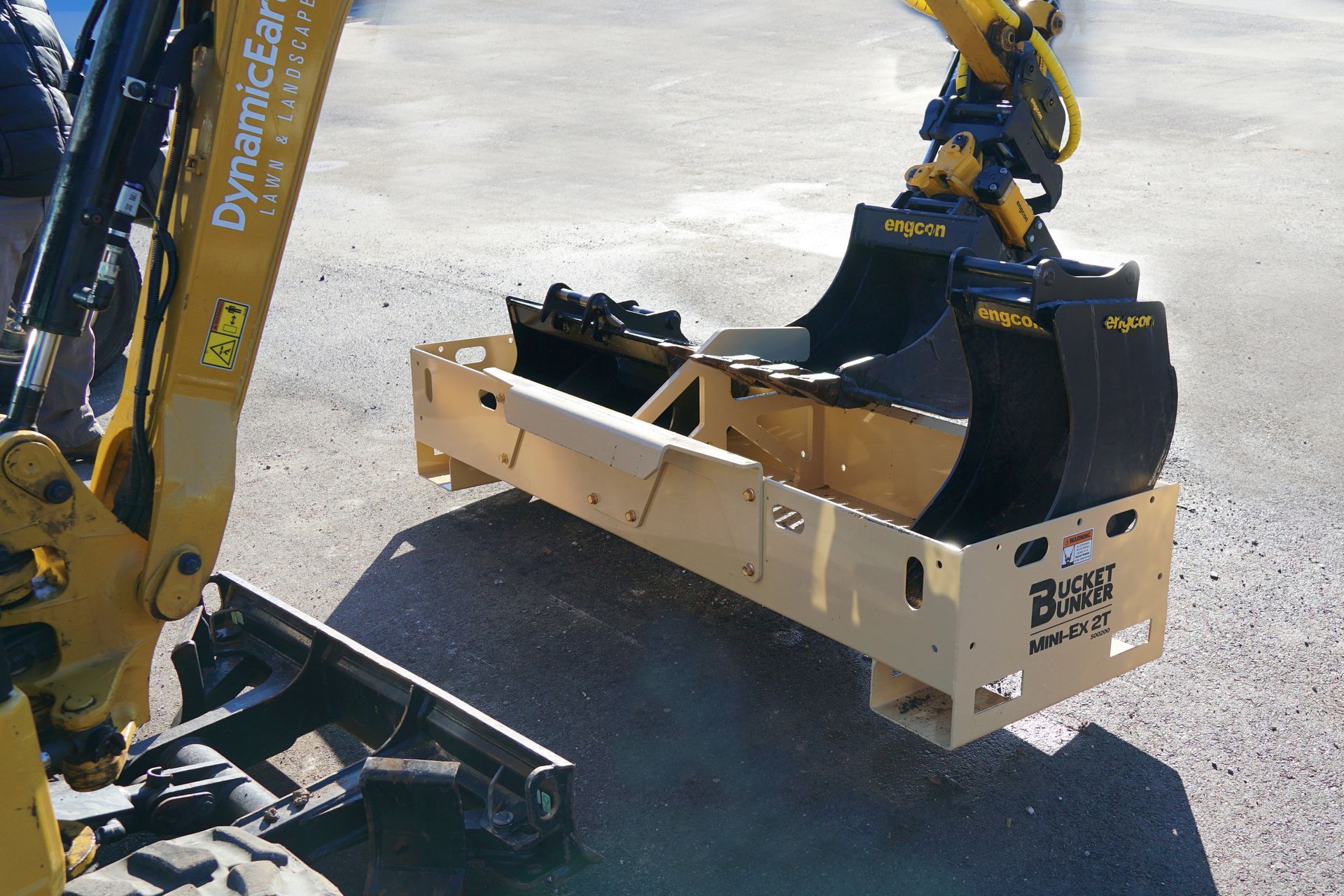 A bucket bunker mini-ex 2t has buckets in it and is sitting Infront of a mini-excavator.