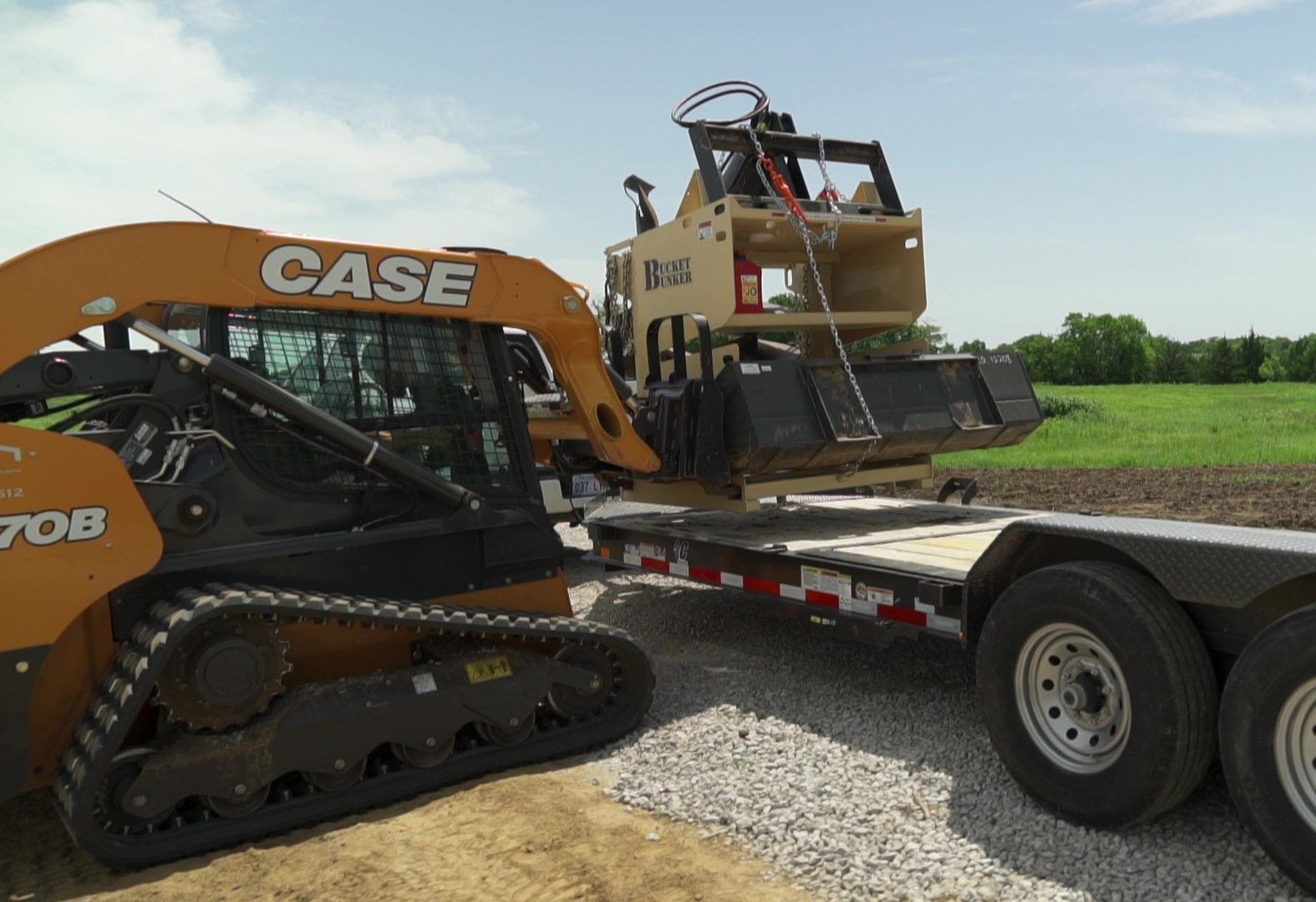 Case skid steer placing a loaded Bucket Bunker on a trailer from the side. 