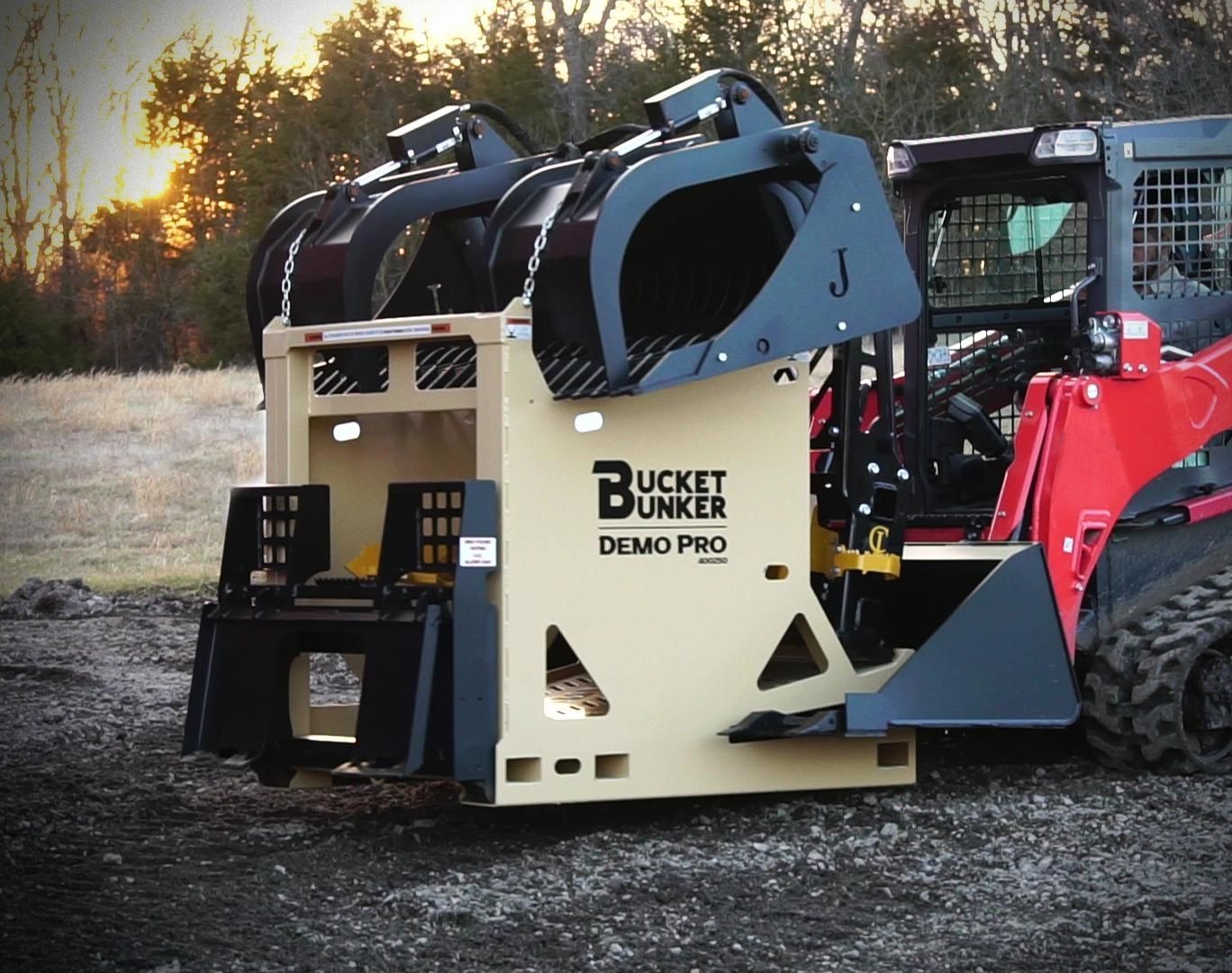 An attachment rack with a grapple bucket, tree puller, & pallet forks,  being transported with the bucket of a skid steer.