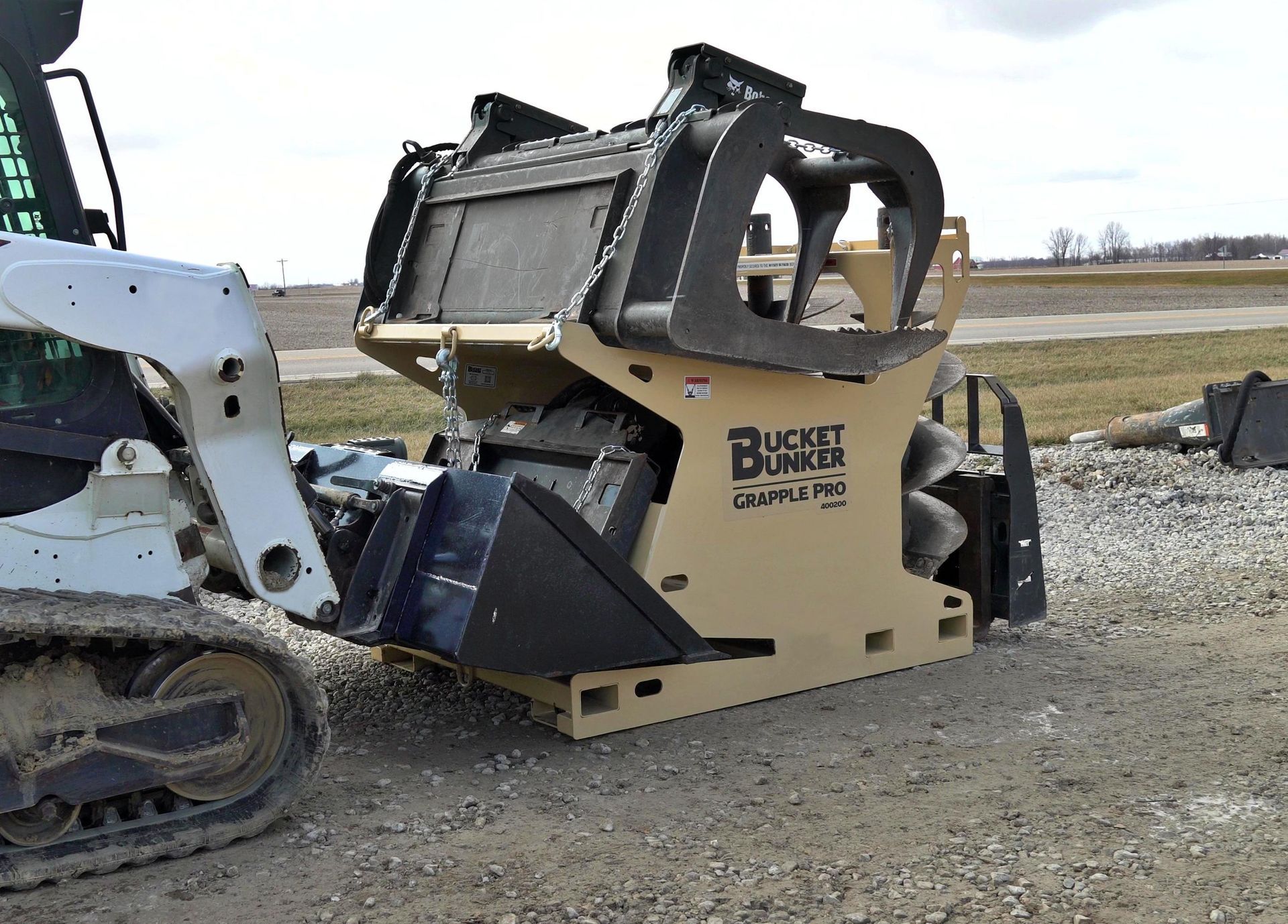 A white skid steer hooking up to a bucket bunker with its loader bucket.