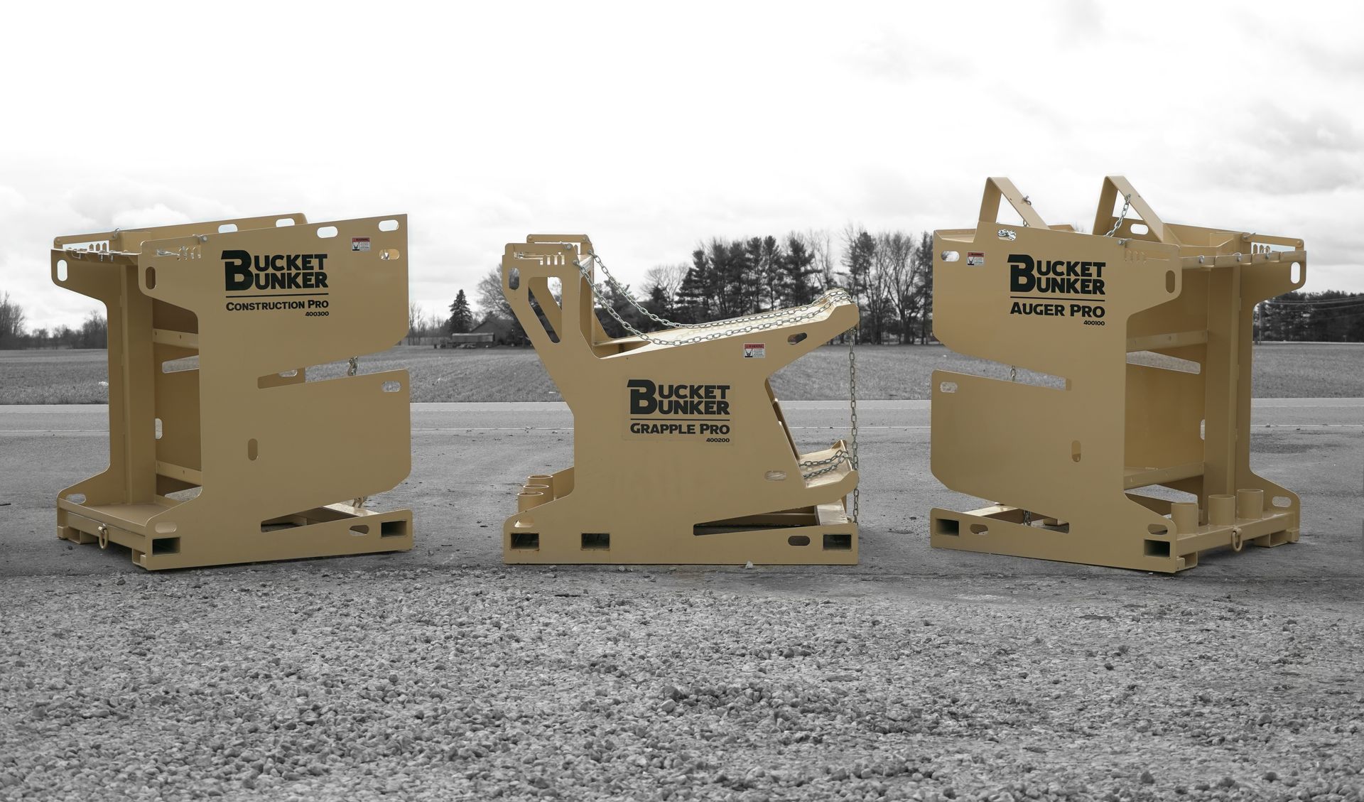 Three bucket bunkers sitting in a gravel lot without attachments on them.  