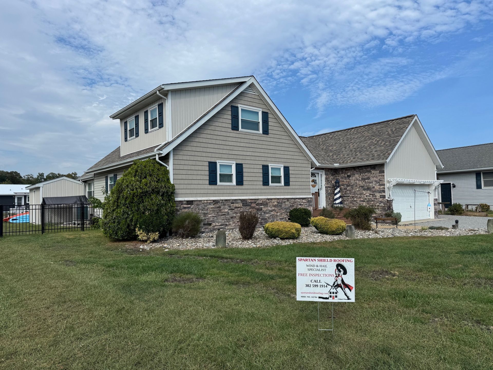 House with tan and gray siding, stone accents, and two-car garage under a blue sky.