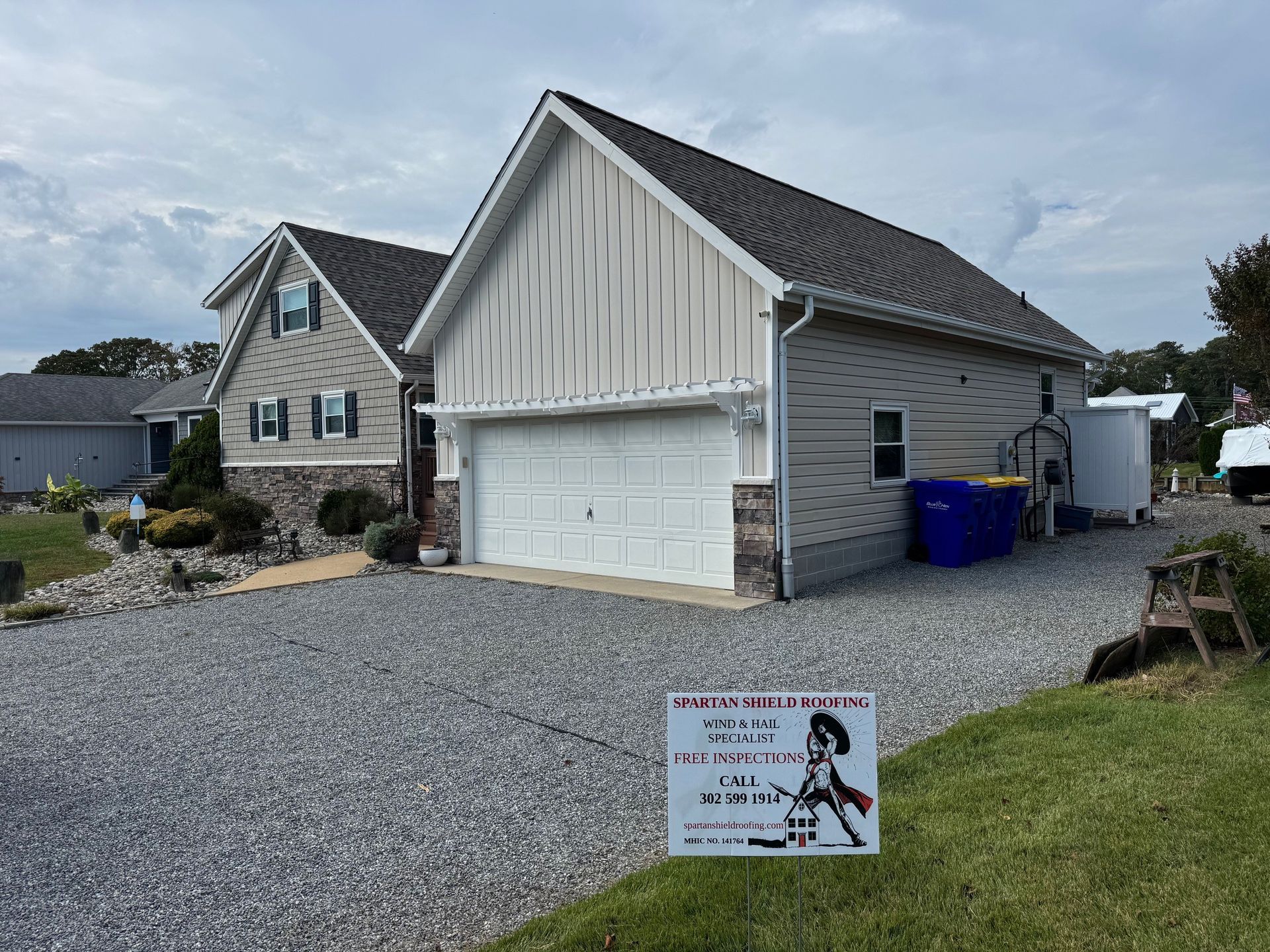 Garage with a white door, light siding, and a sign on the grass. Gray gravel driveway.