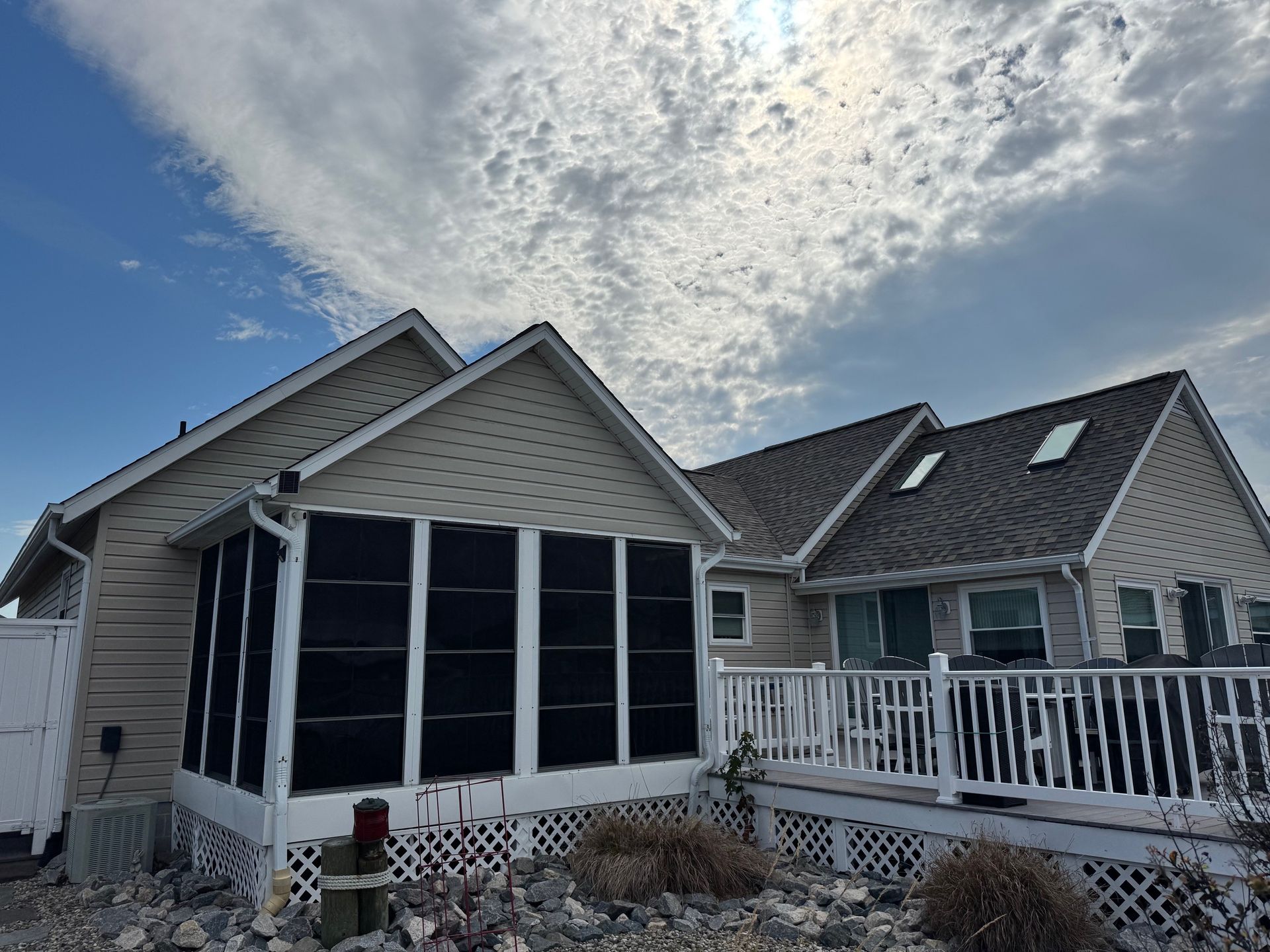 House with screened-in porch, white trim, deck, and gray roof, under a cloudy blue sky.
