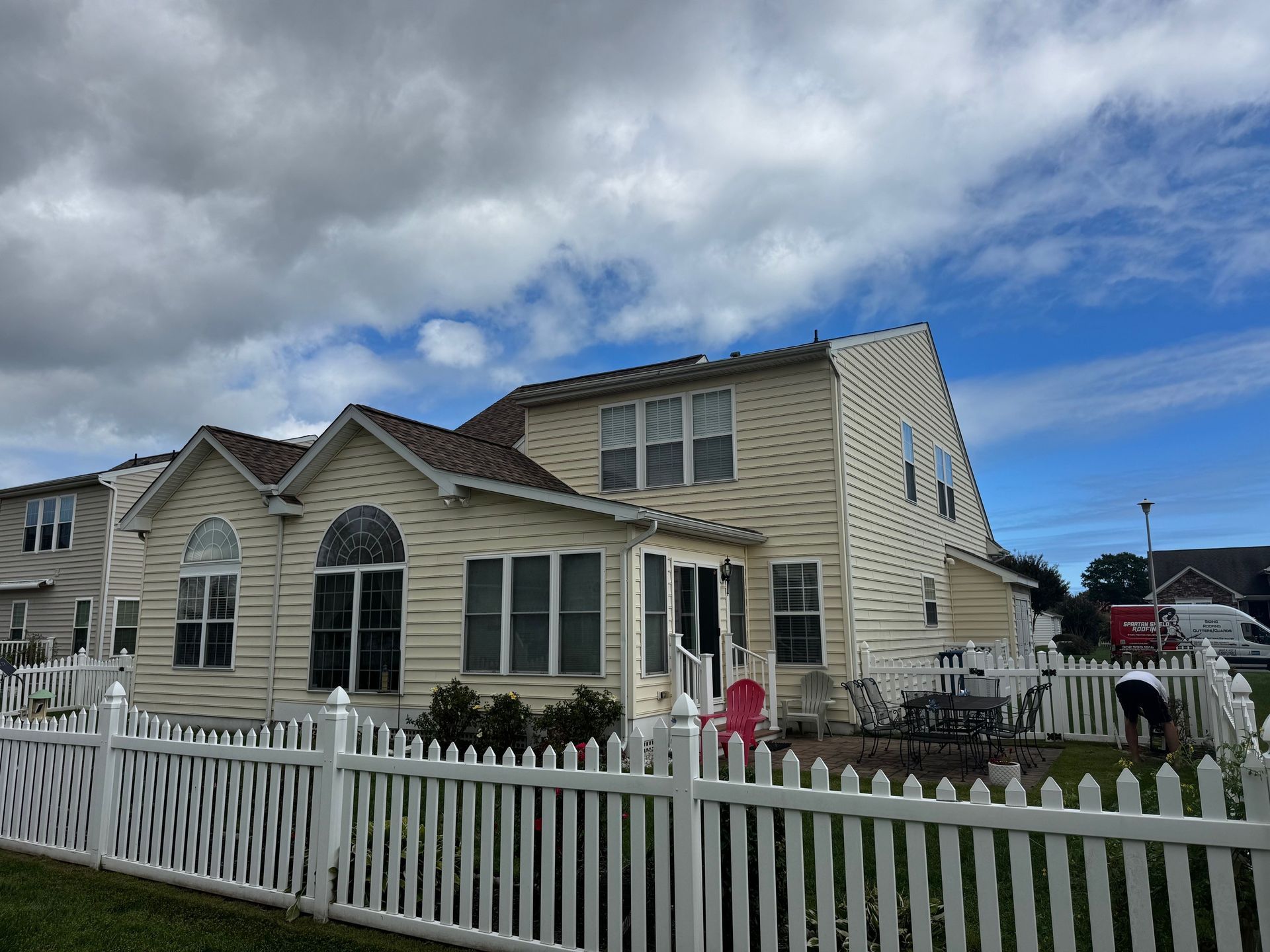 Beige house with a white picket fence under a cloudy sky.