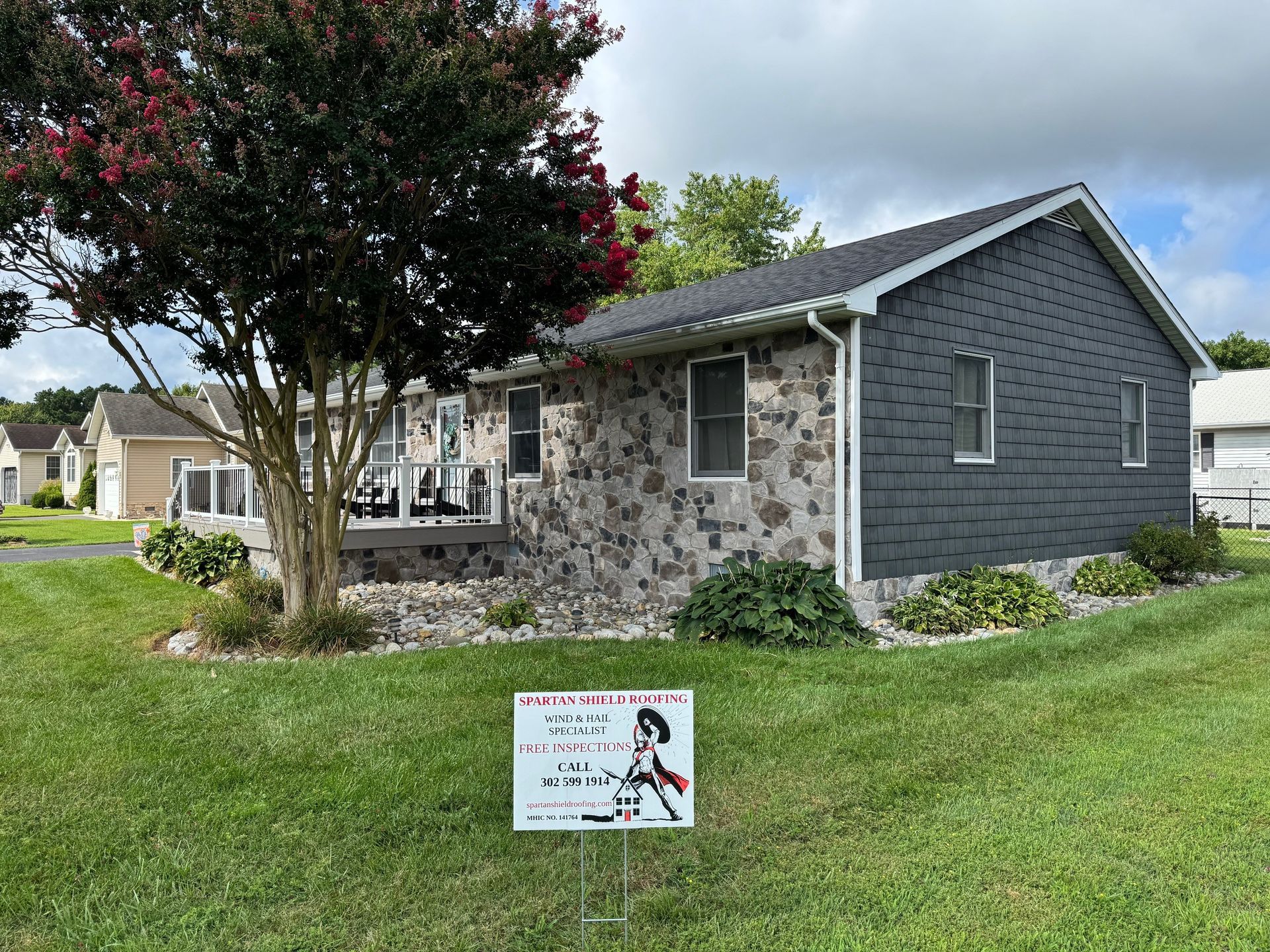 House with stone and gray siding, small yard, sign in front, cloudy day.