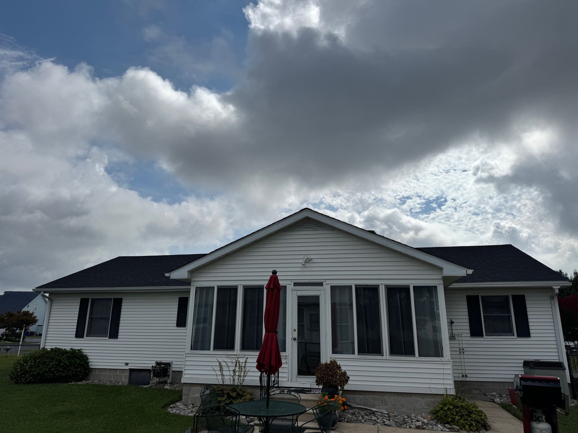 White house with black roof and screened-in porch under cloudy sky. Red umbrella on the porch.