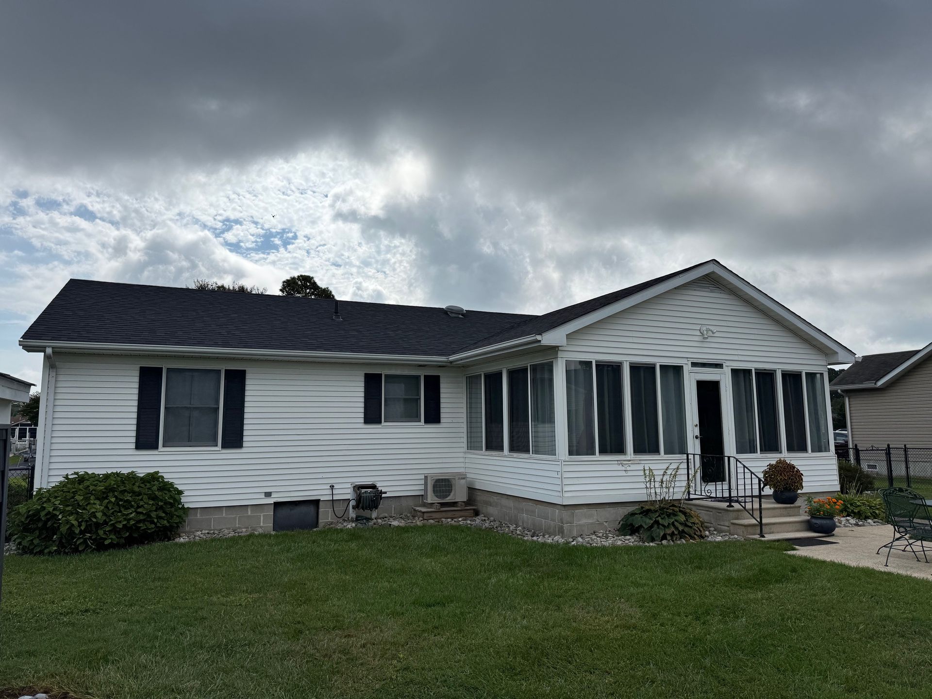 White ranch-style house with dark roof and screened porch under a cloudy sky.