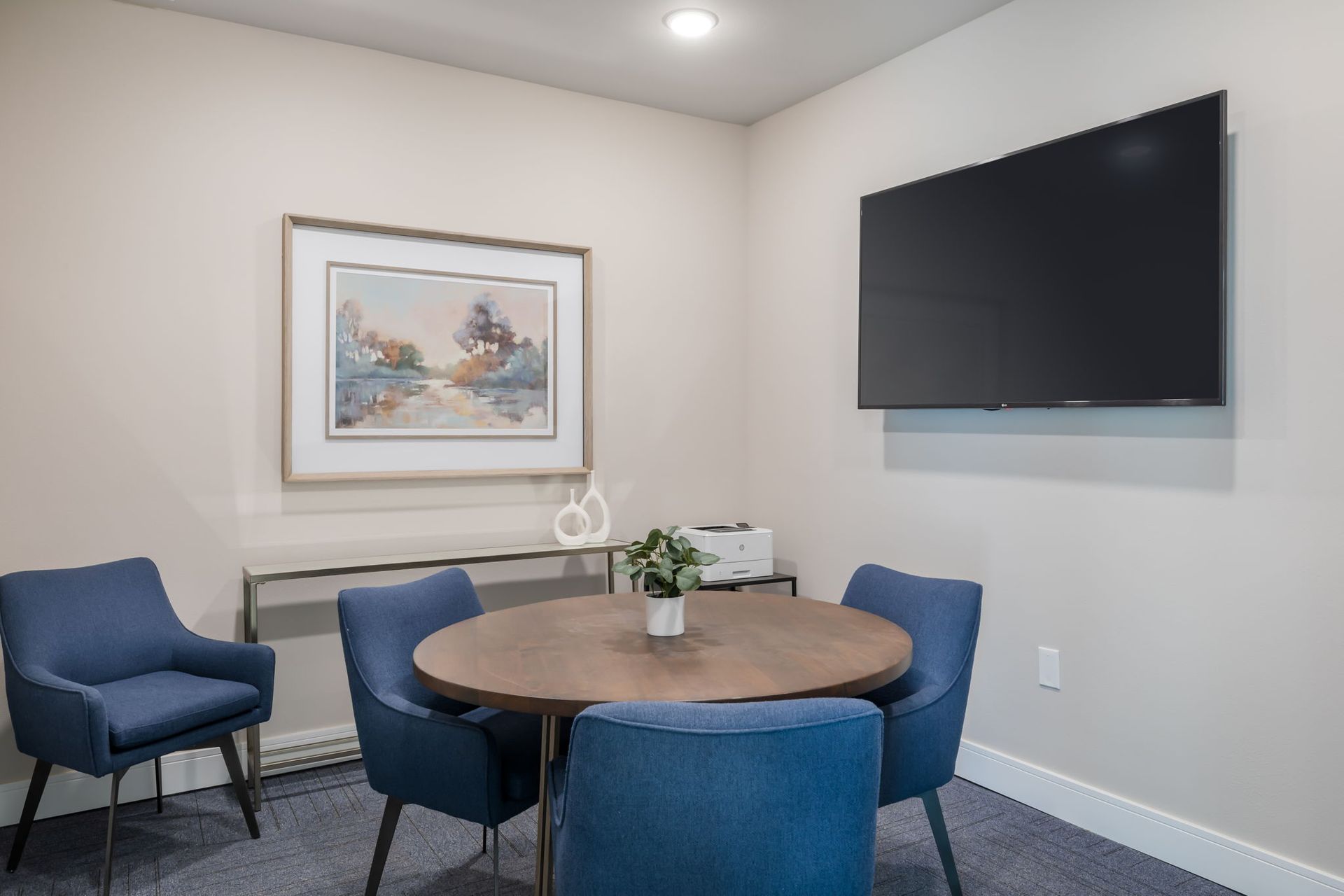 A conference room with a round table and chairs and a flat screen tv.