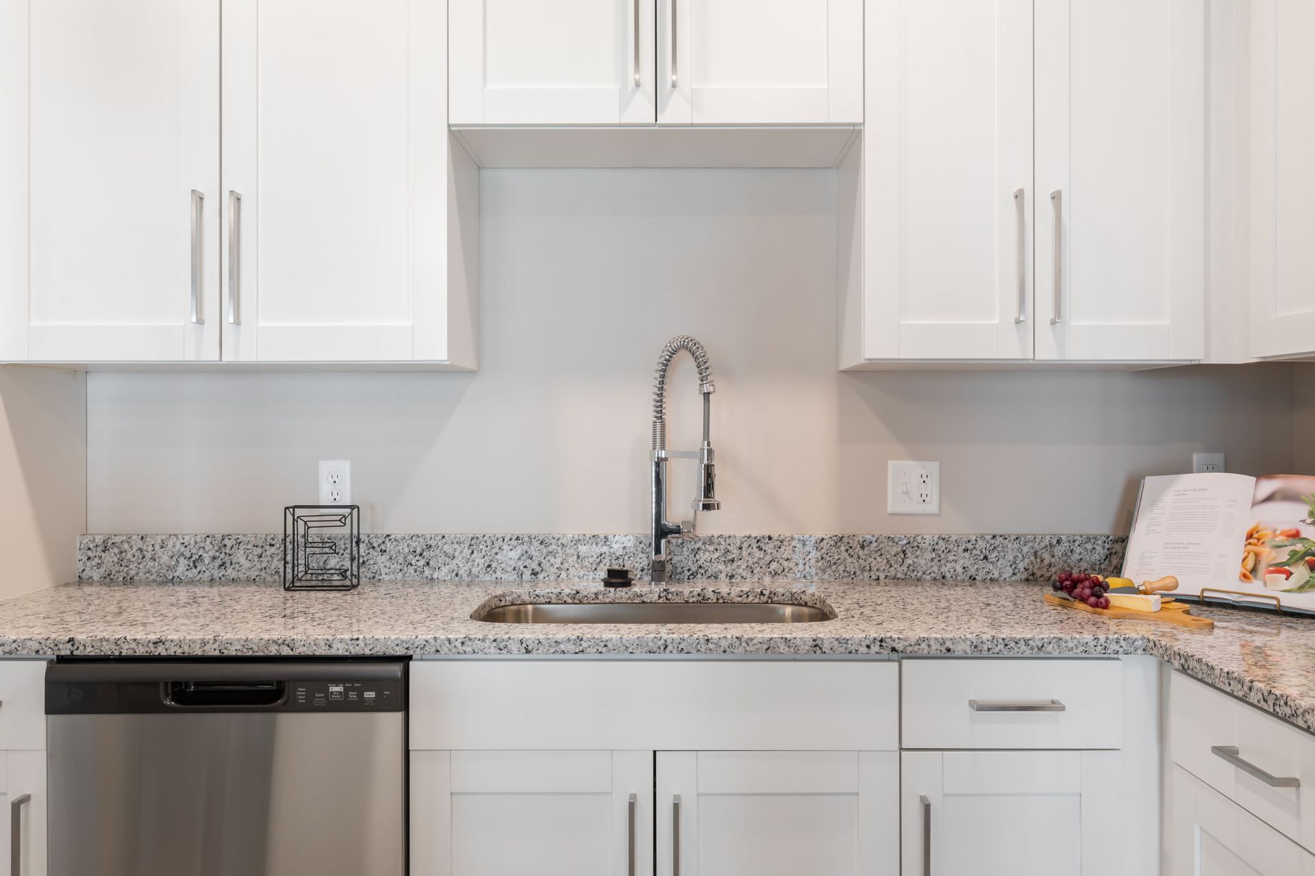 A kitchen with white cabinets , granite counter tops , a sink , and a stainless steel dishwasher.