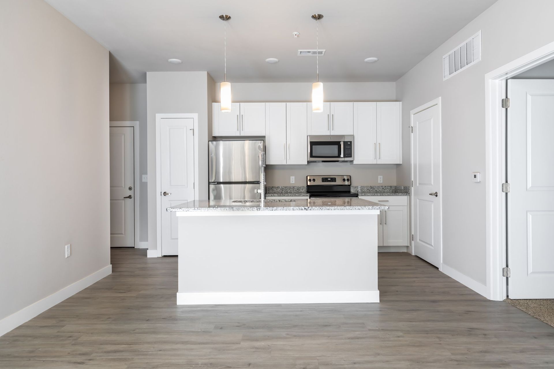 An empty kitchen with white cabinets , stainless steel appliances , and a large island.