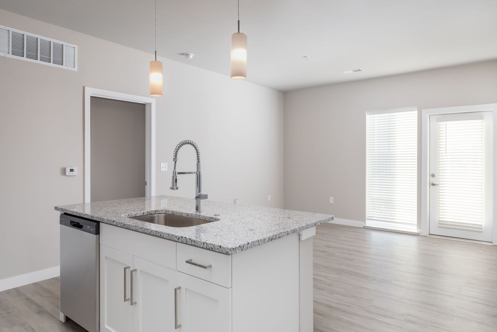 An empty kitchen with a sink , dishwasher , and sliding glass doors.