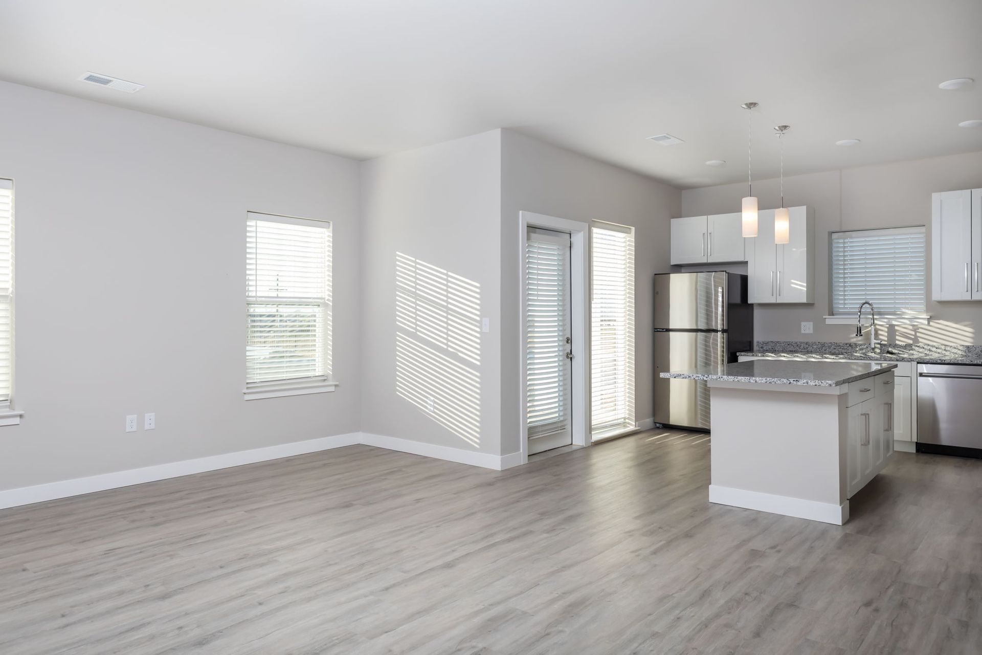 An empty living room with a kitchen in the background.