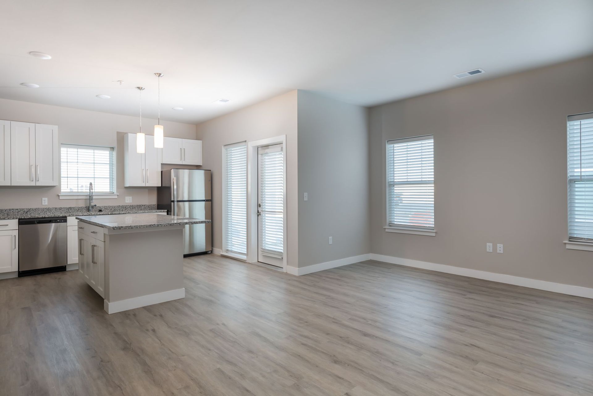 A living room with hardwood floors and a kitchen with stainless steel appliances.