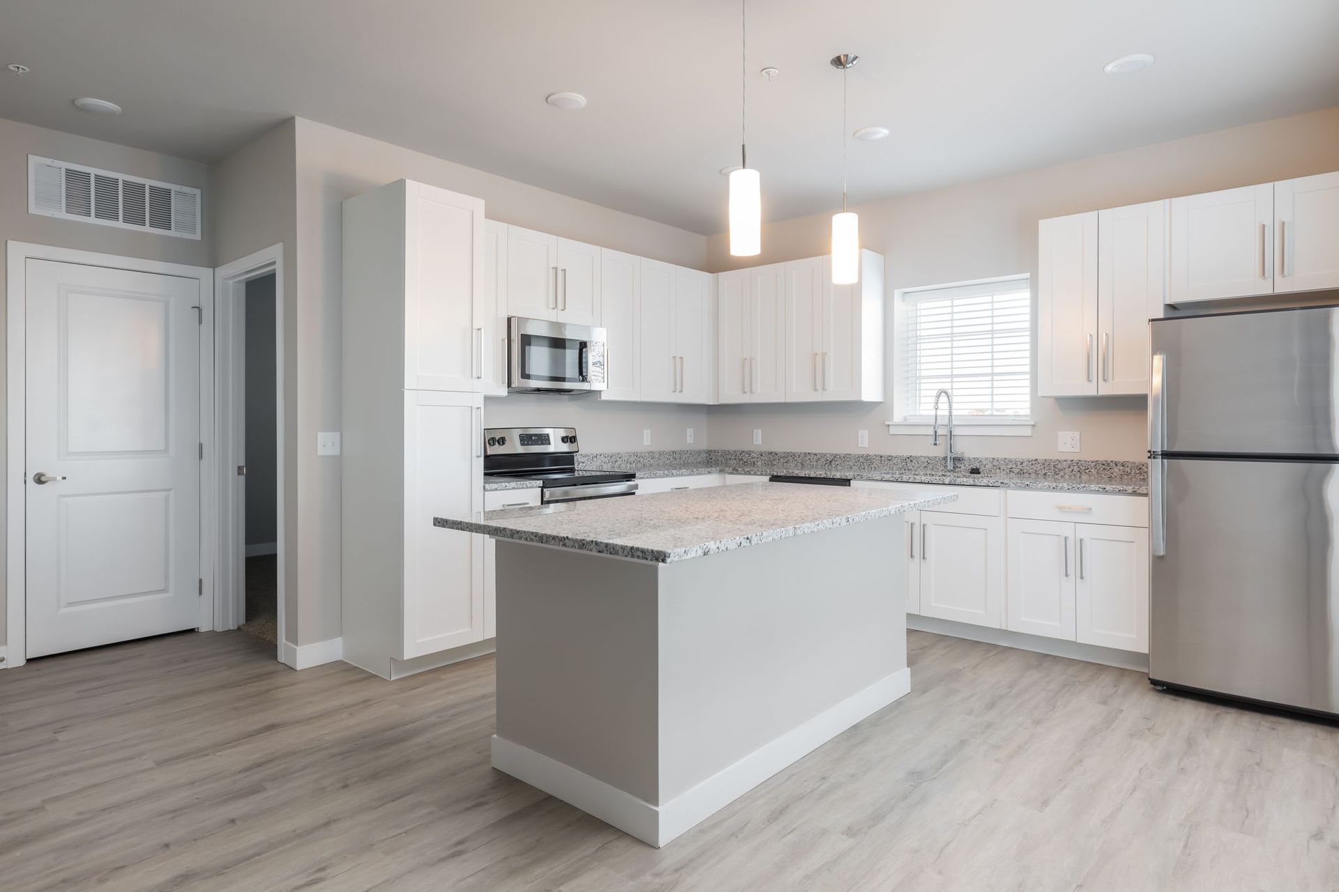 A kitchen with white cabinets , stainless steel appliances , and a large island.