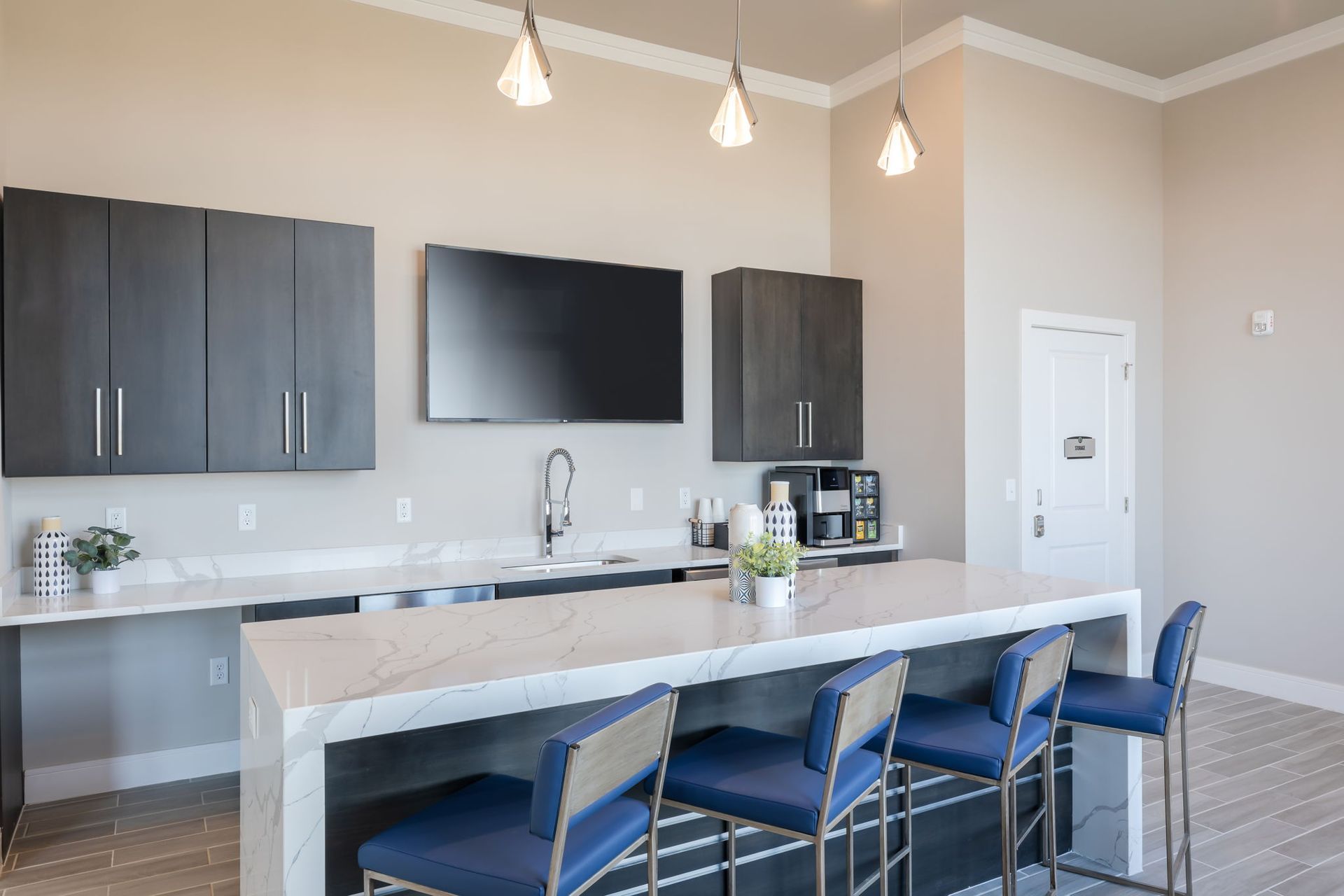 A kitchen with a long counter and stools and a flat screen tv.