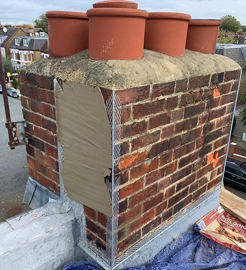 Rooftop brick chimney with four red pots, partially covered in protective sheeting and fresh mortar.