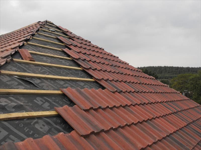 Roof under construction with red tiles being installed over black underlayment on a steep house roof
