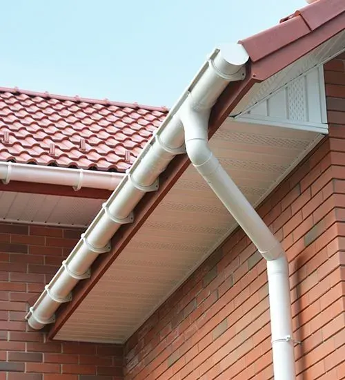 White rain gutter and downspout on a red-tiled brick house under the eaves