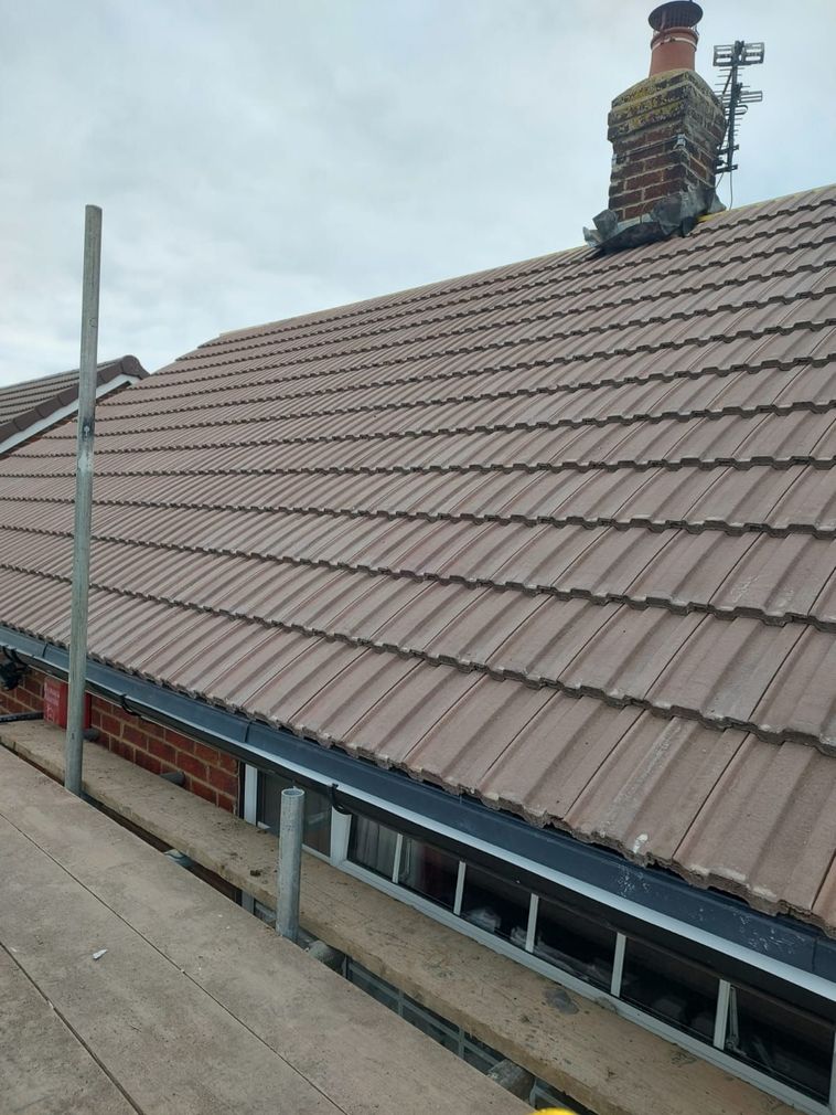 Tiled roof with a chimney beside a rooftop walkway under a cloudy sky