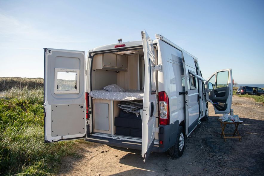 White campervan parked with doors open, revealing bed and storage.