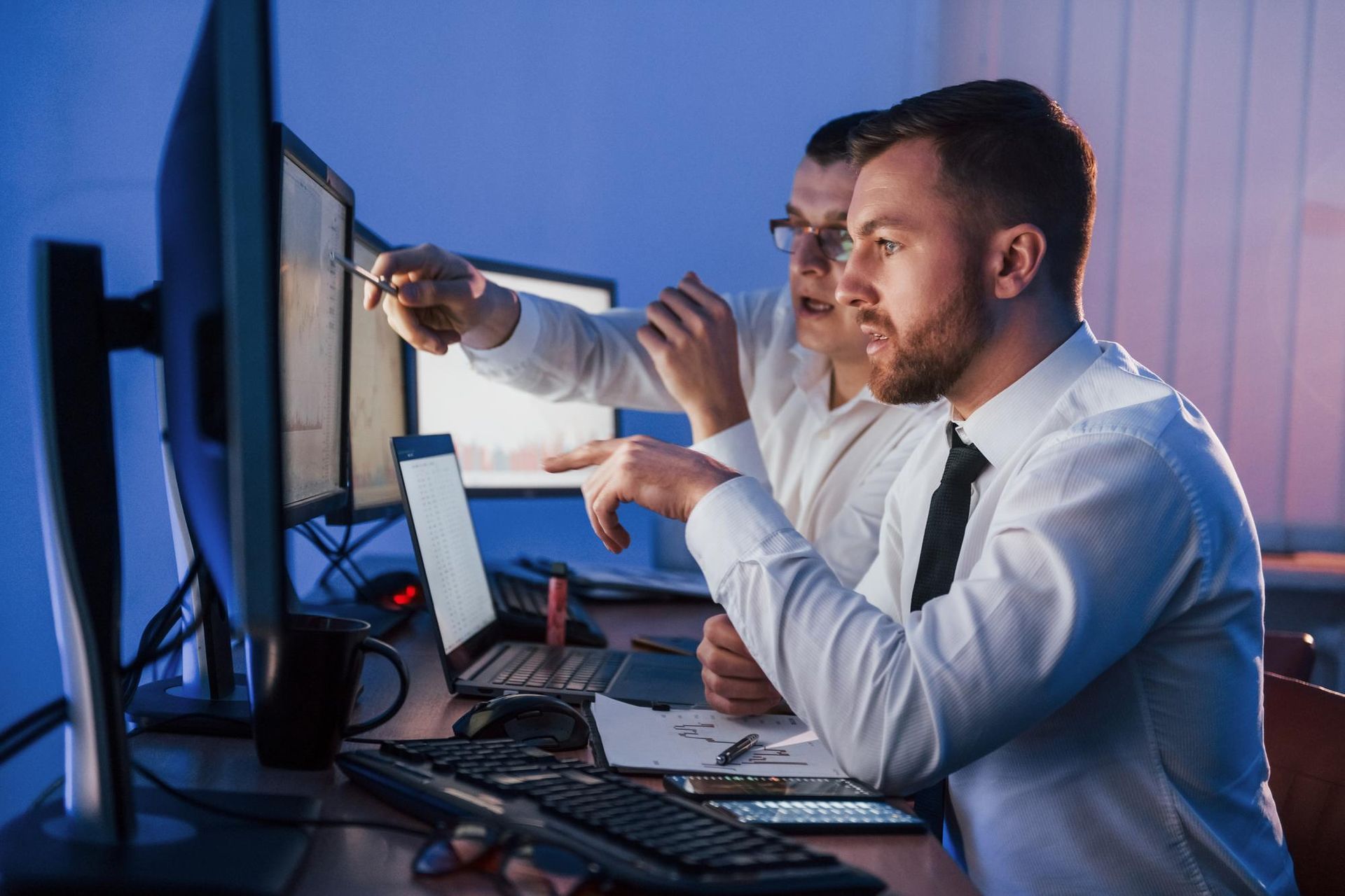 Two men are sitting at a desk looking at a computer screen.