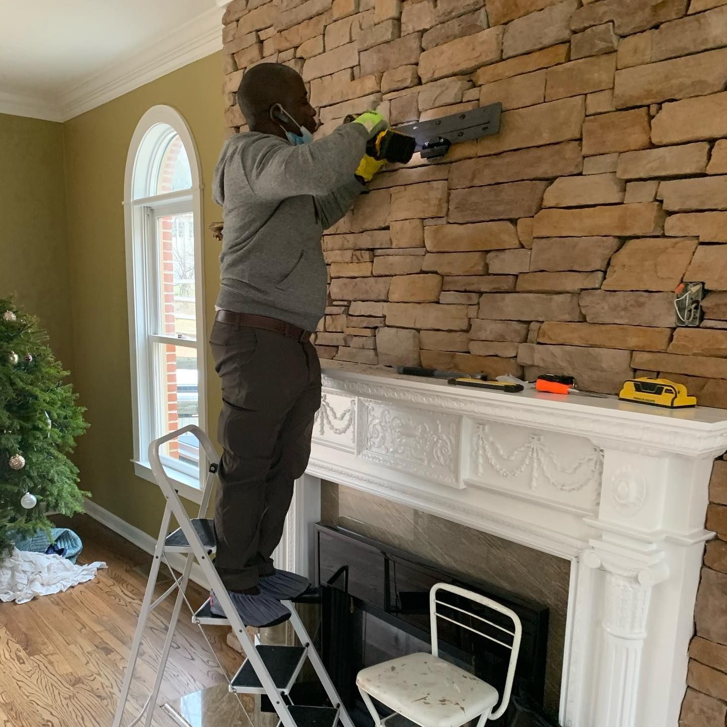 Person using a saw on a stone wall, standing on a step ladder near a fireplace.