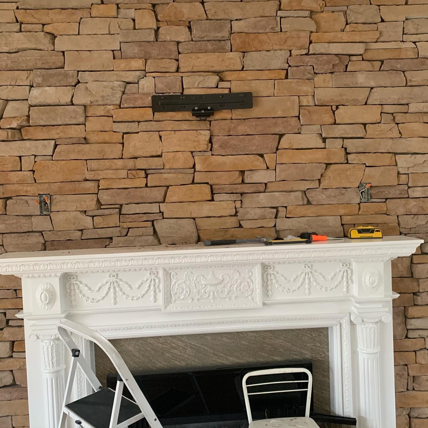 Stone wall with a white fireplace, a TV mount, and tools.