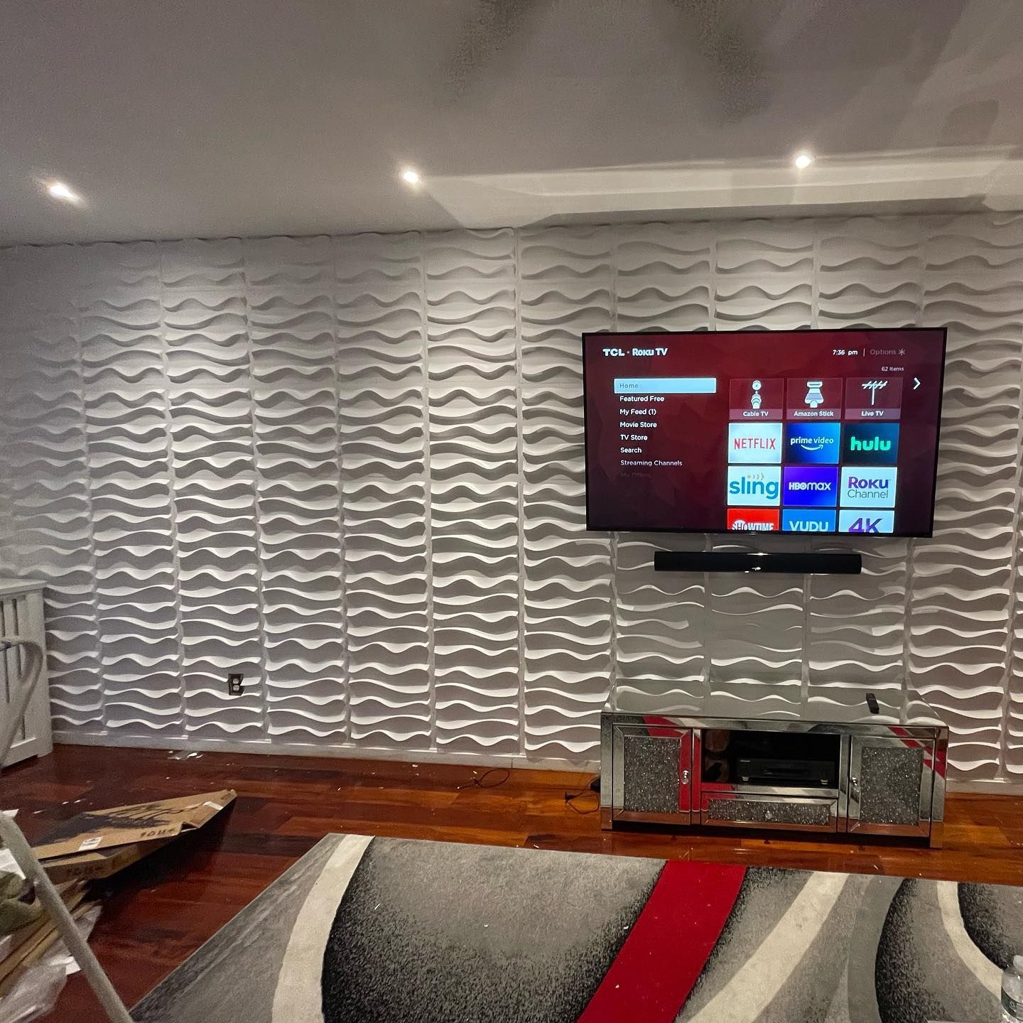 Living room with textured white wall, TV, soundbar, silver console, rug, and hardwood floor.