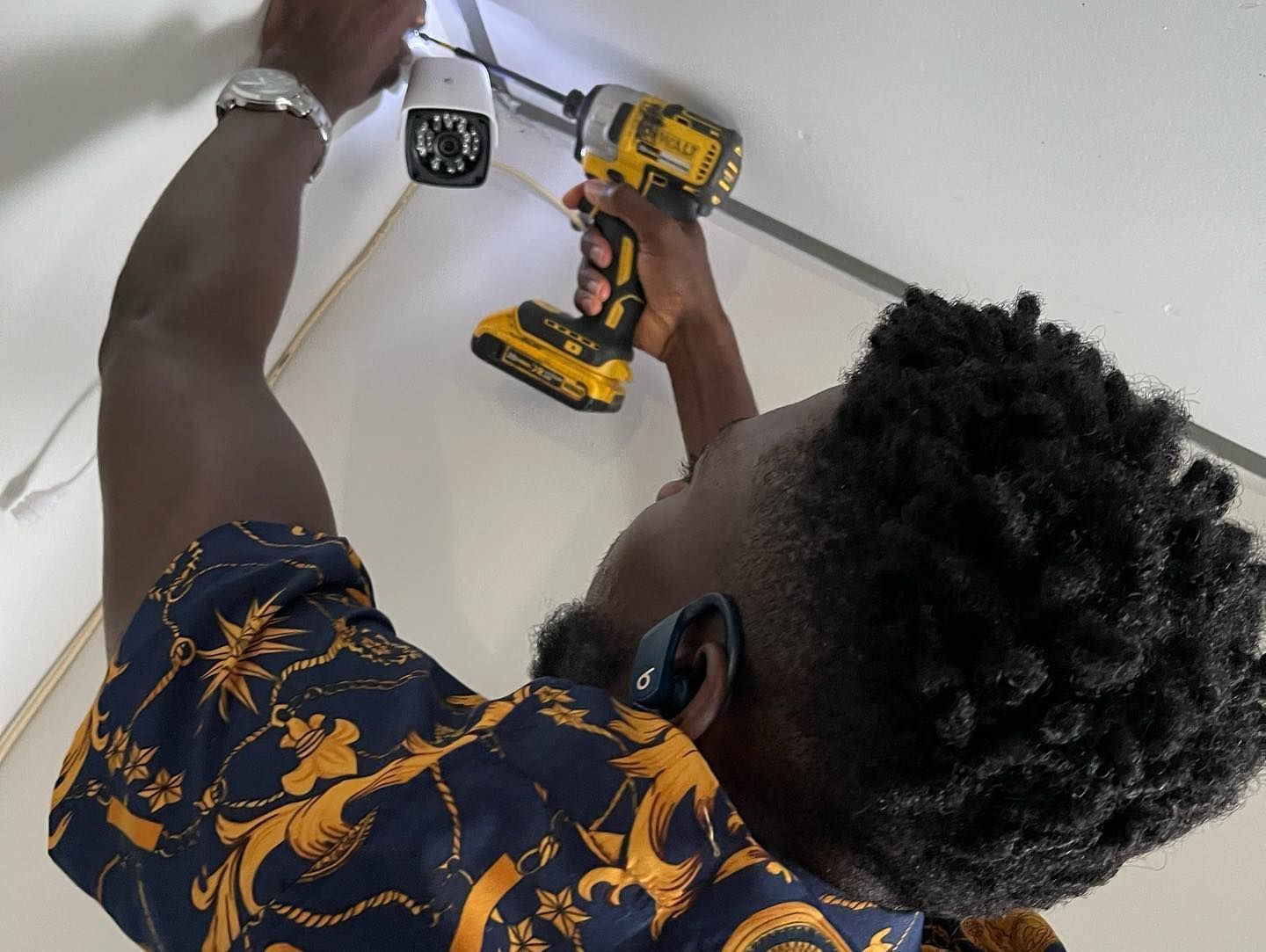 Person installs security camera with a drill on a white ceiling.