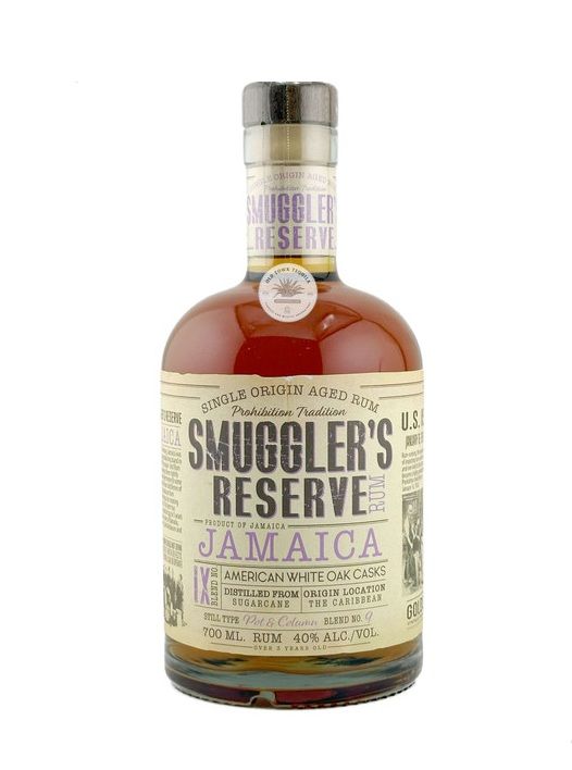 Bottle of Smuggler's Reserve Jamaica Rum, amber liquid, vintage label, clear glass, white background.