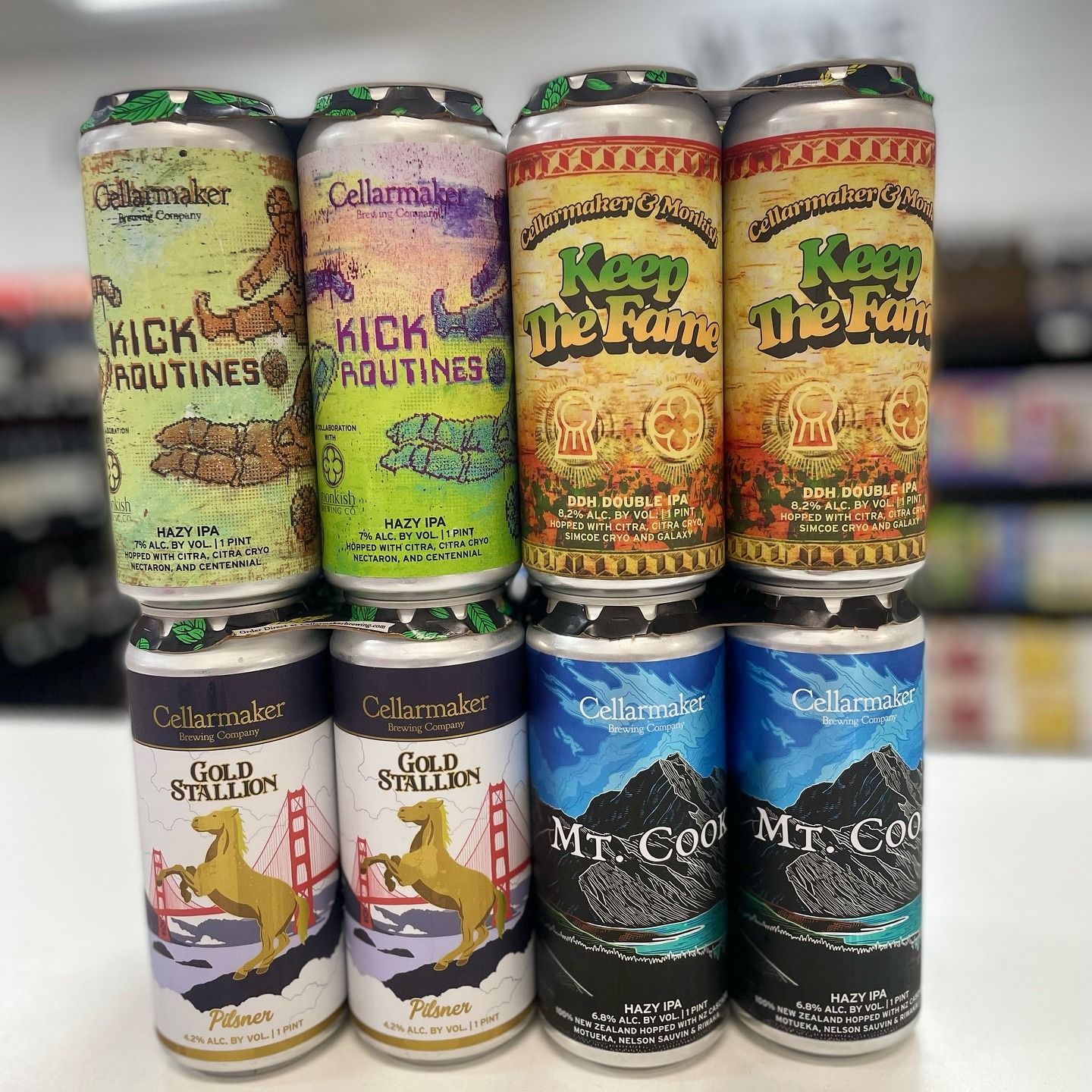 Eight colorful beer cans stacked, featuring different labels with text and illustrations.