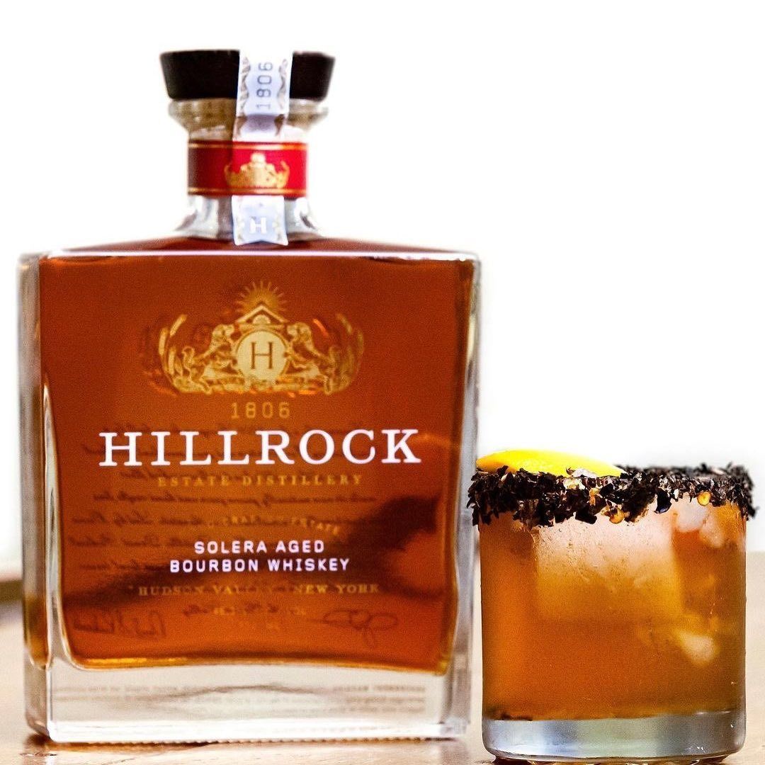 Bottle of Hillrock bourbon whiskey next to a cocktail with a garnished rim.