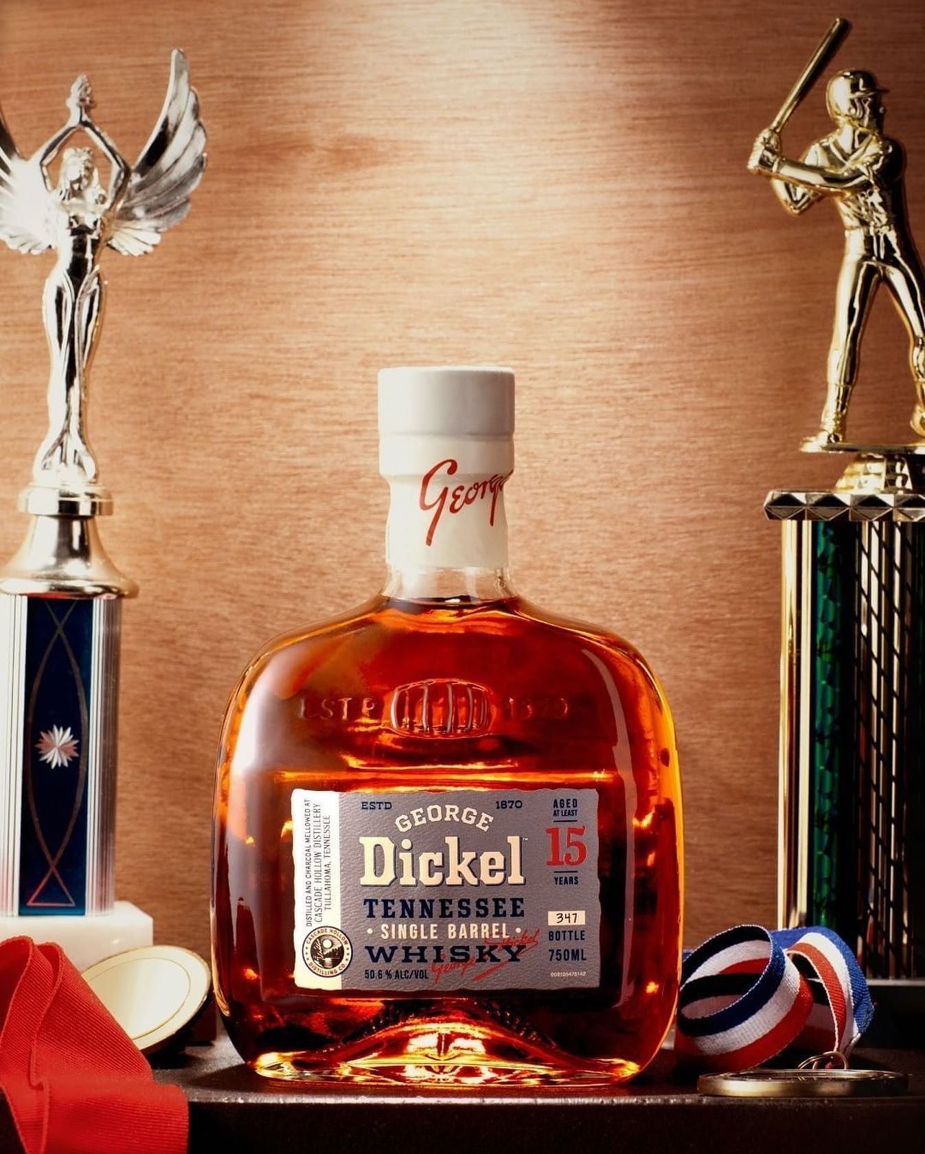 Bottle of George Dickel 15-year-old Tennessee Whiskey, trophy, medals, baseball statue on a wooden surface.