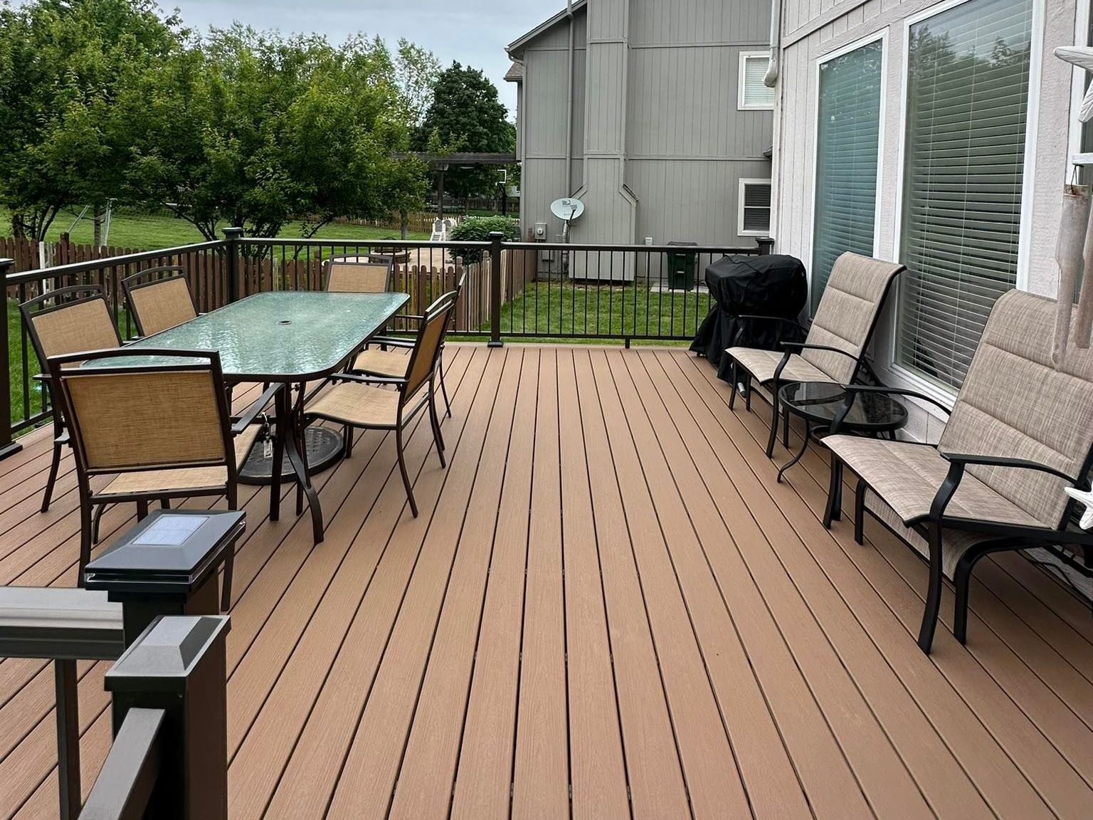 Wooden deck with outdoor furniture, including a table with chairs and lounge chairs near the house.