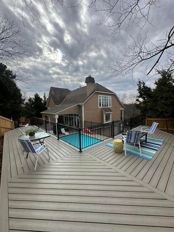 Backyard with pool, deck, and house under a cloudy sky. Furnished deck, black fence.