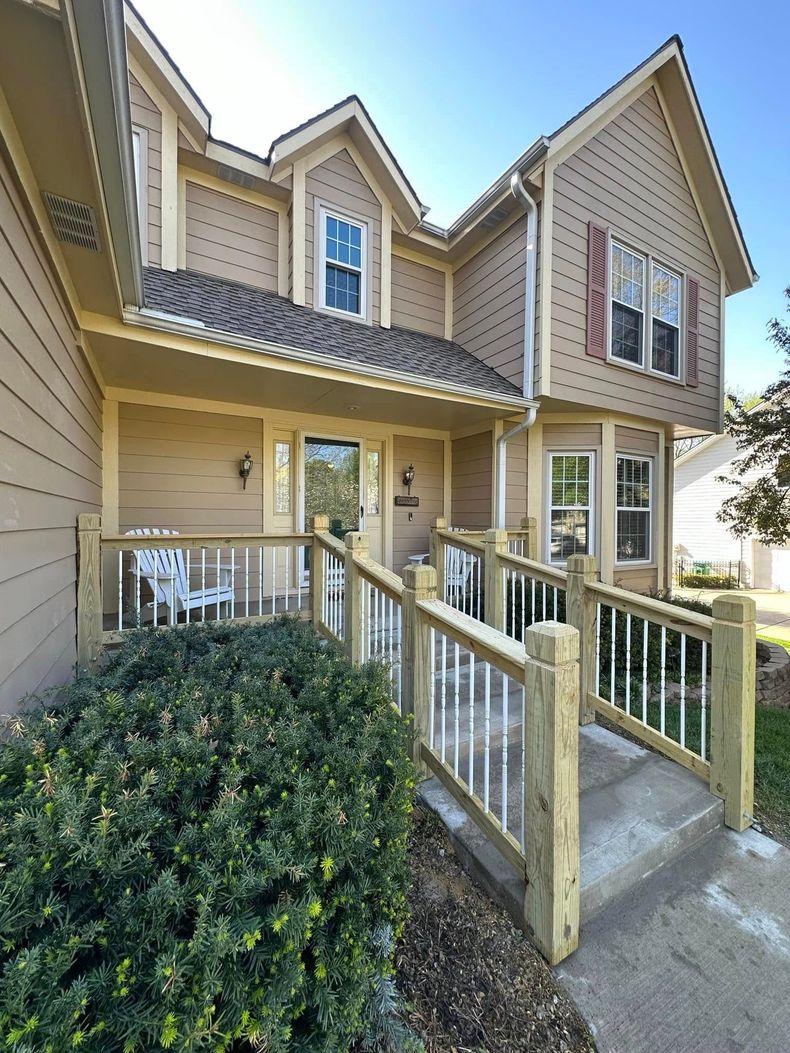Exterior view of a two-story beige townhouse with a ramp leading to the front door. Sunny day.