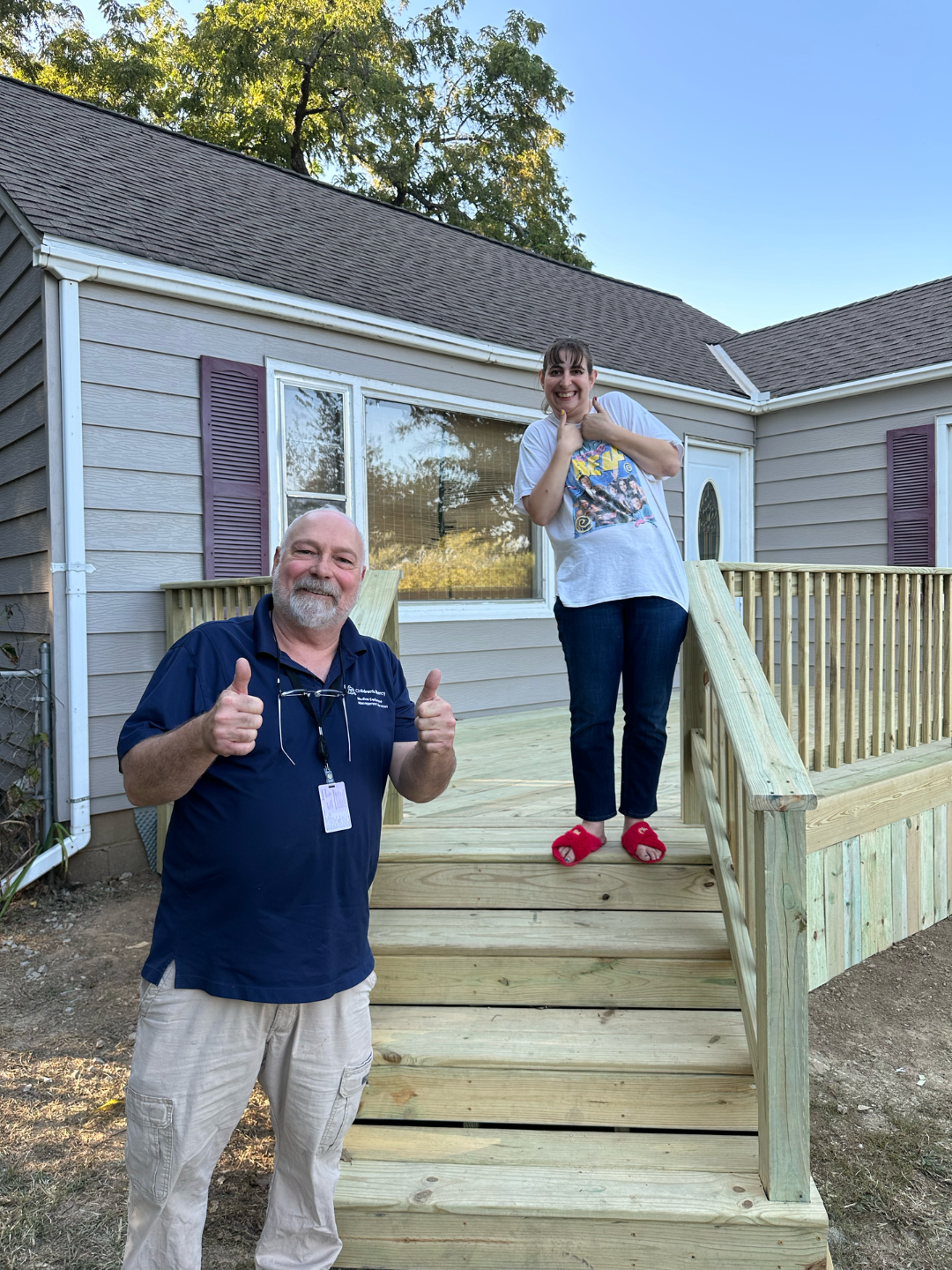 Man and woman on new wooden deck in front of house. Man gives thumbs-up, woman smiles excitedly.