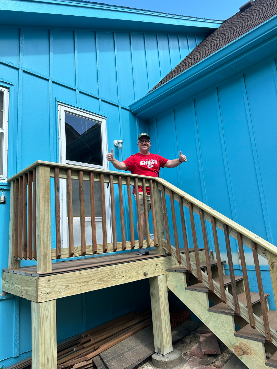 Man on new wooden deck, blue house exterior. Giving thumbs up.