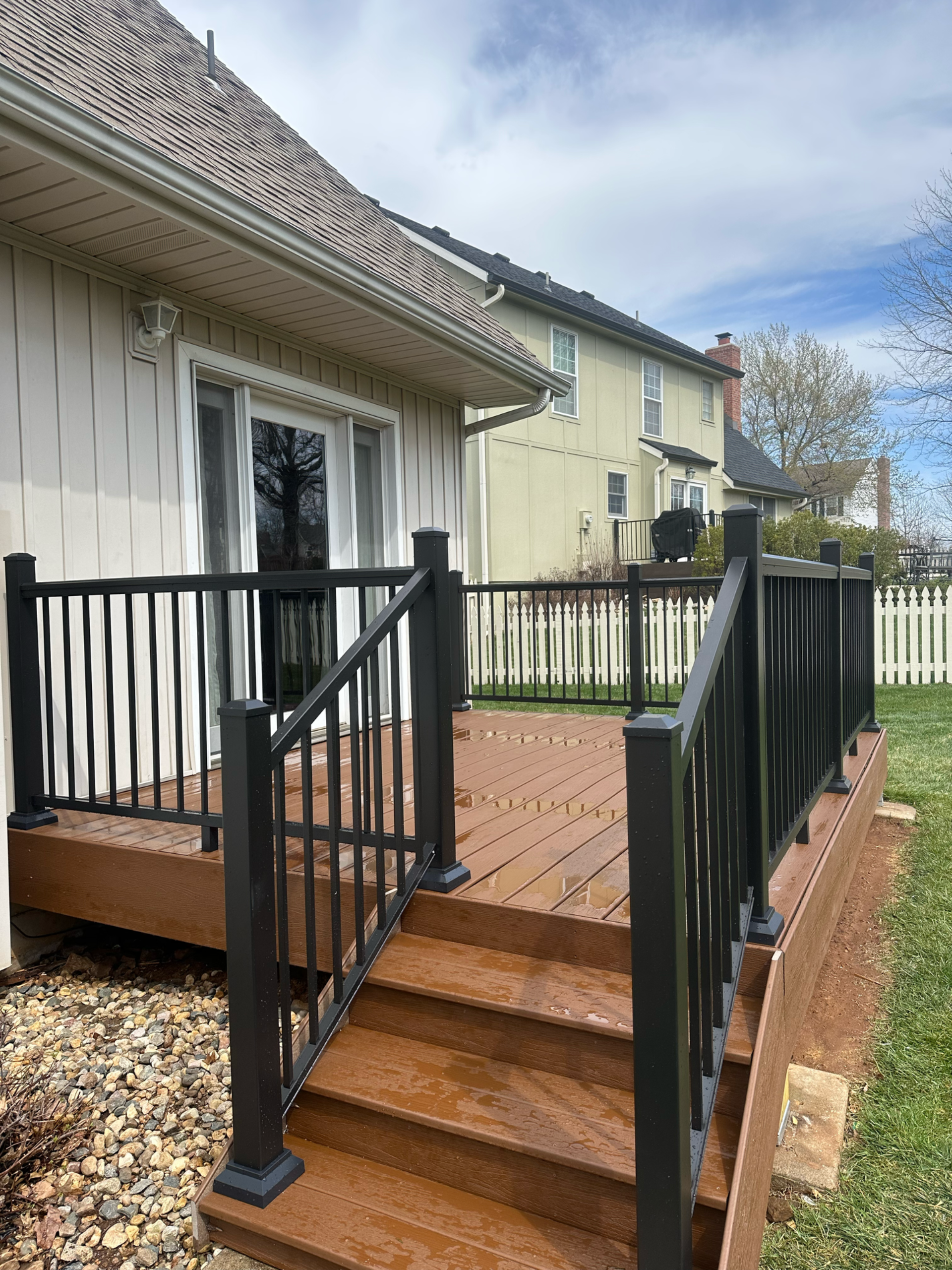 Wooden deck with black railing, steps leading down to a grassy yard. Beige house in background.