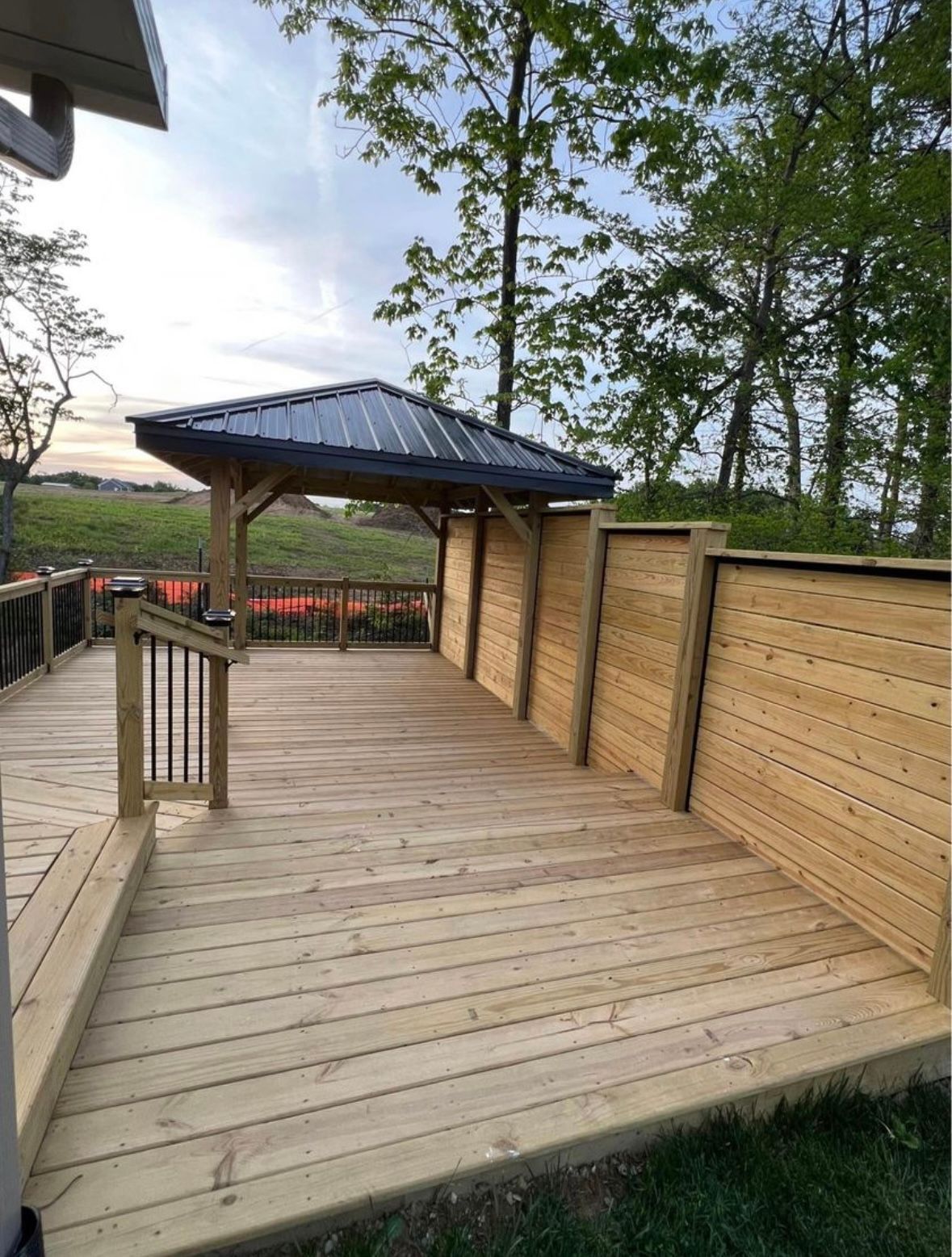 Wooden deck with gazebo, fence, and railing. Overcast sky and trees in the background.