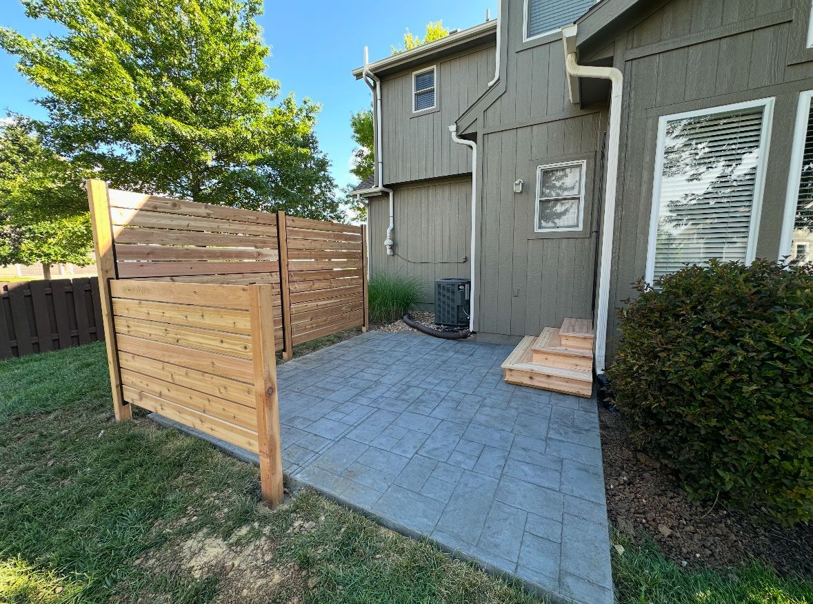 Patio with gray pavers, wooden privacy fence, and house with steps and air conditioner.