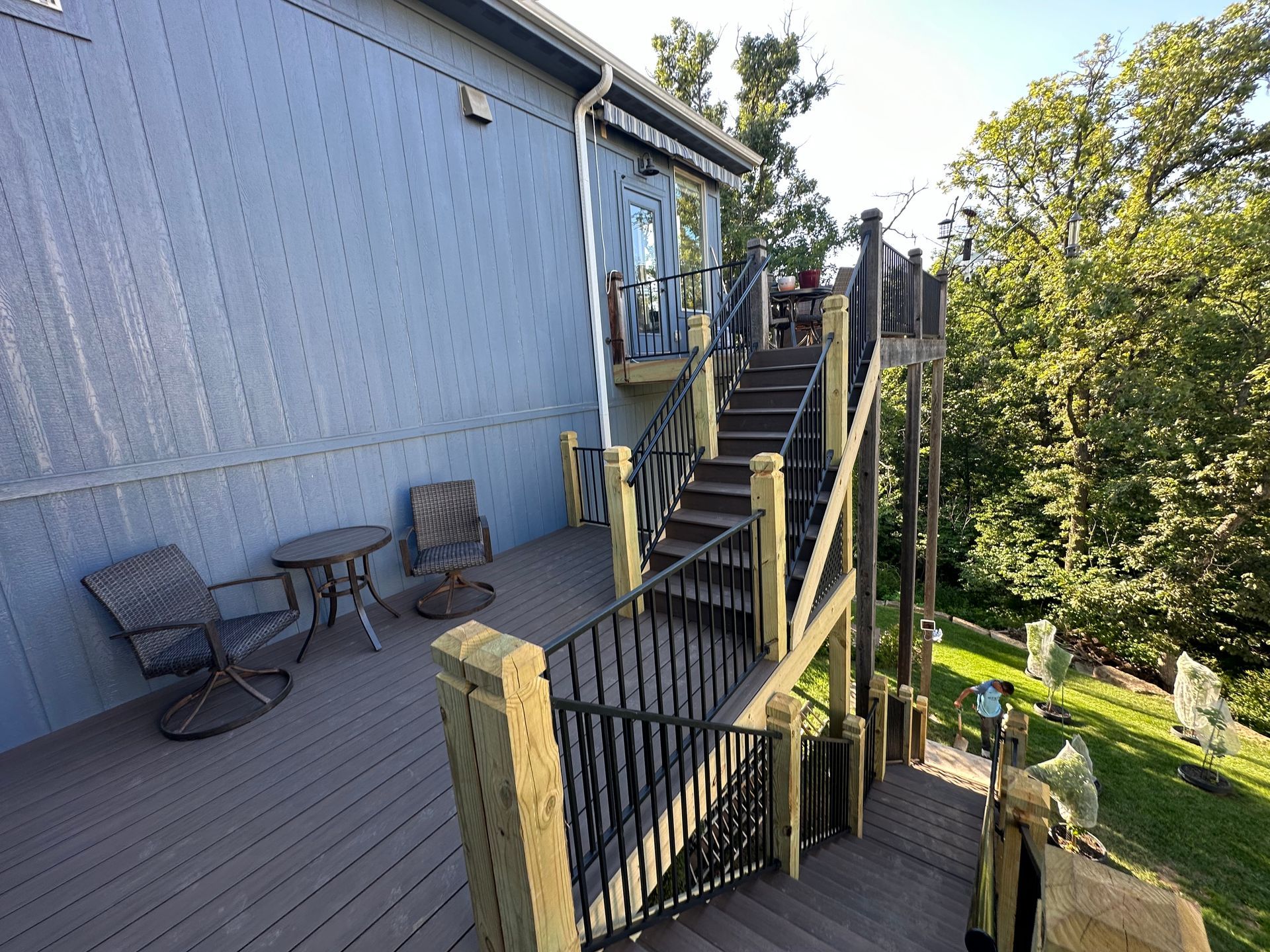 A blue house with a deck and stairs leading up to a higher level.