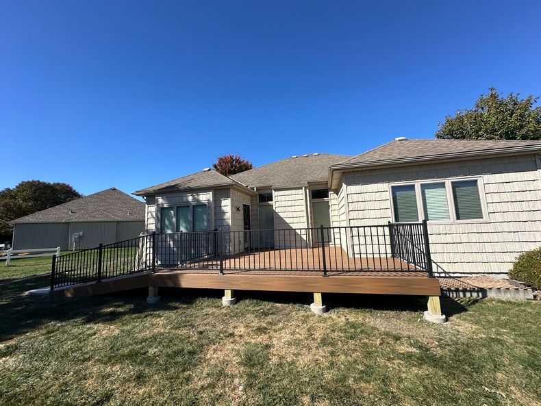 Backyard view of a house with a wooden deck and a wheelchair ramp on a sunny day.