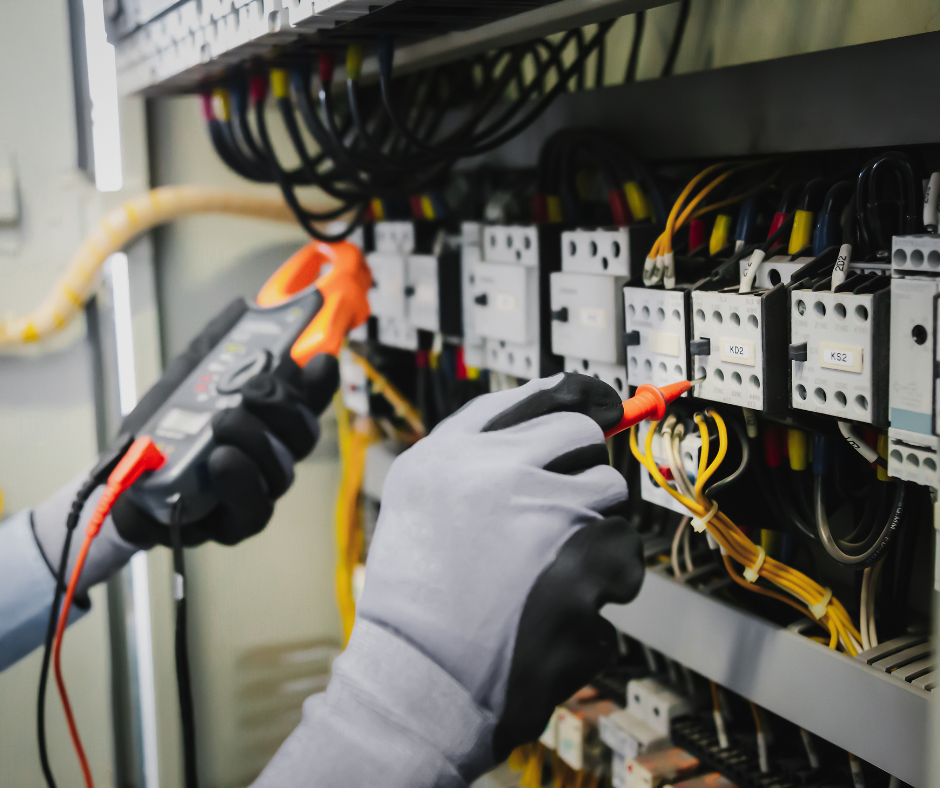 An electrician is working on an electrical panel with a multimeter.